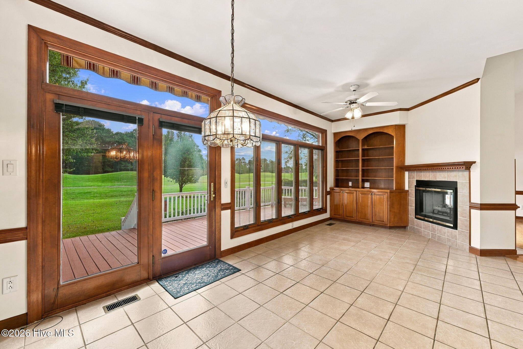 Sunroom with a tiled floor, built-in shelving, fireplace, and glass doors opening to a deck and lawn.