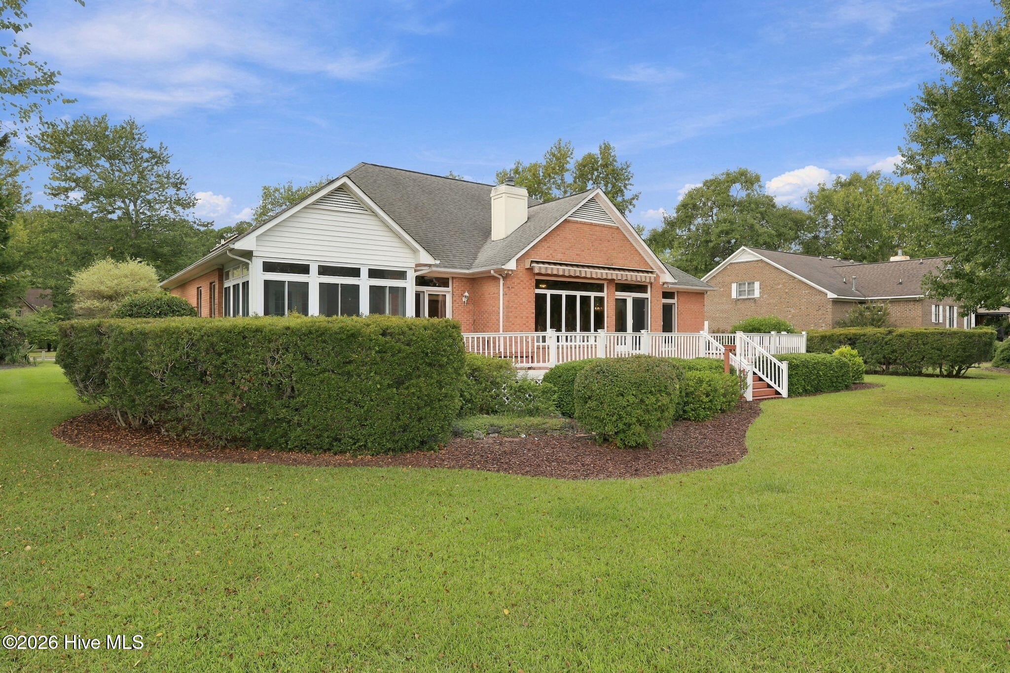 Brick home with a white-railed deck, trimmed shrubs, and a broad green lawn.
