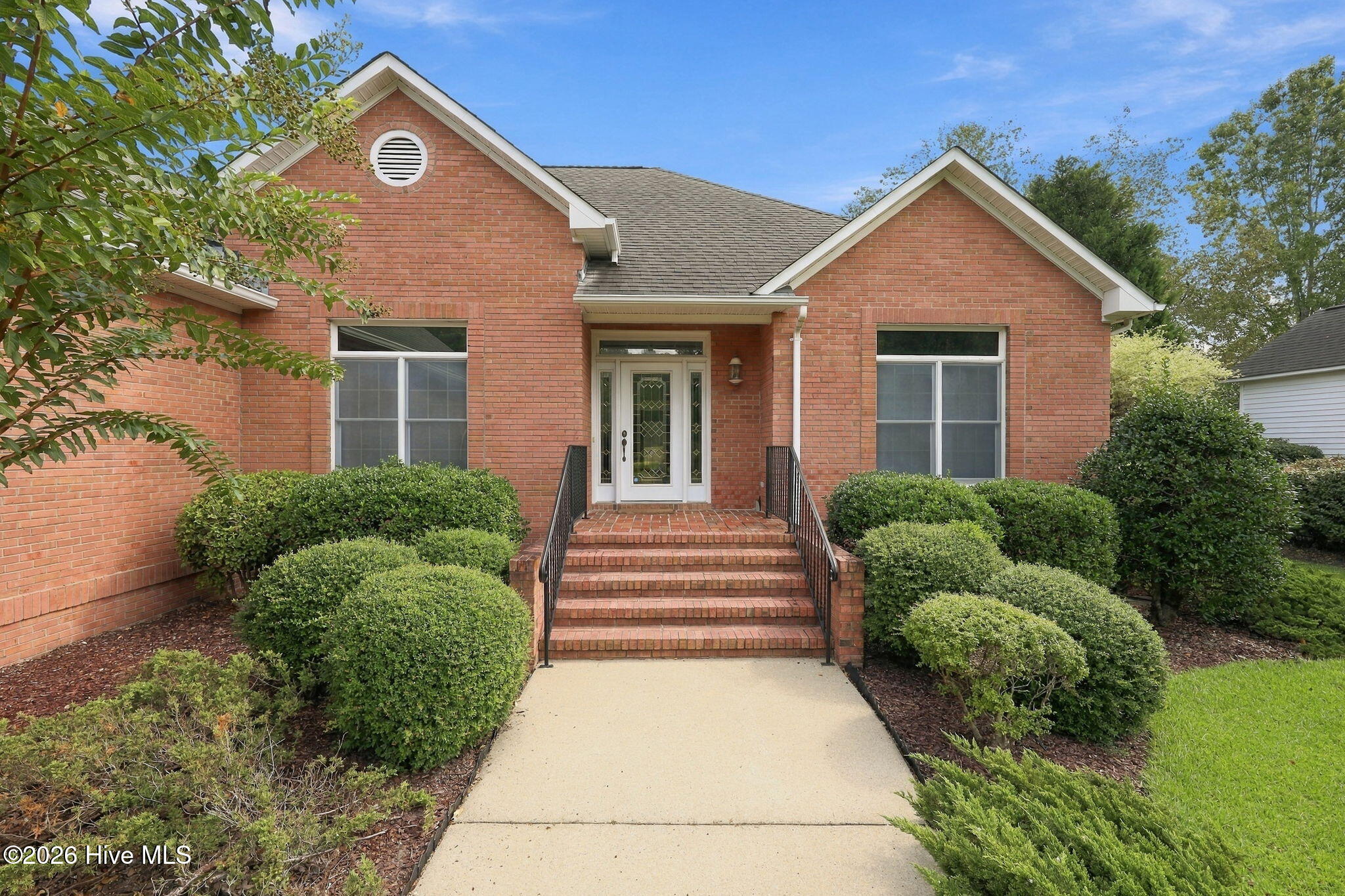 Red-brick house with a gabled facade, brick entry steps, and landscaped shrubs along the walkway.
