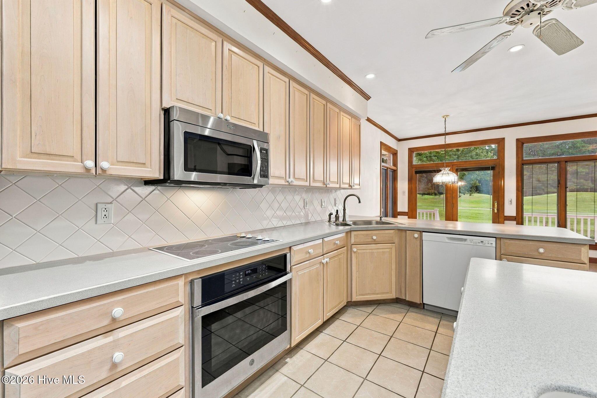 Kitchen with pale wood cabinets, stainless steel appliances, and windows overlooking a lawn.
