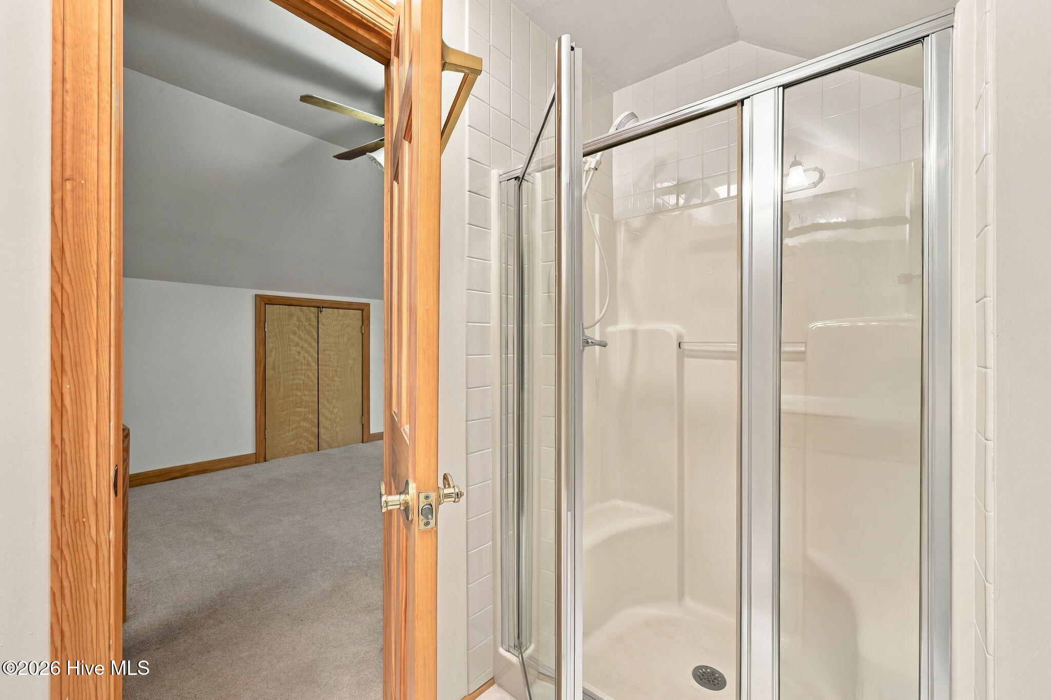 Bathroom shower with glass doors beside a wood-trimmed doorway to a carpeted room.