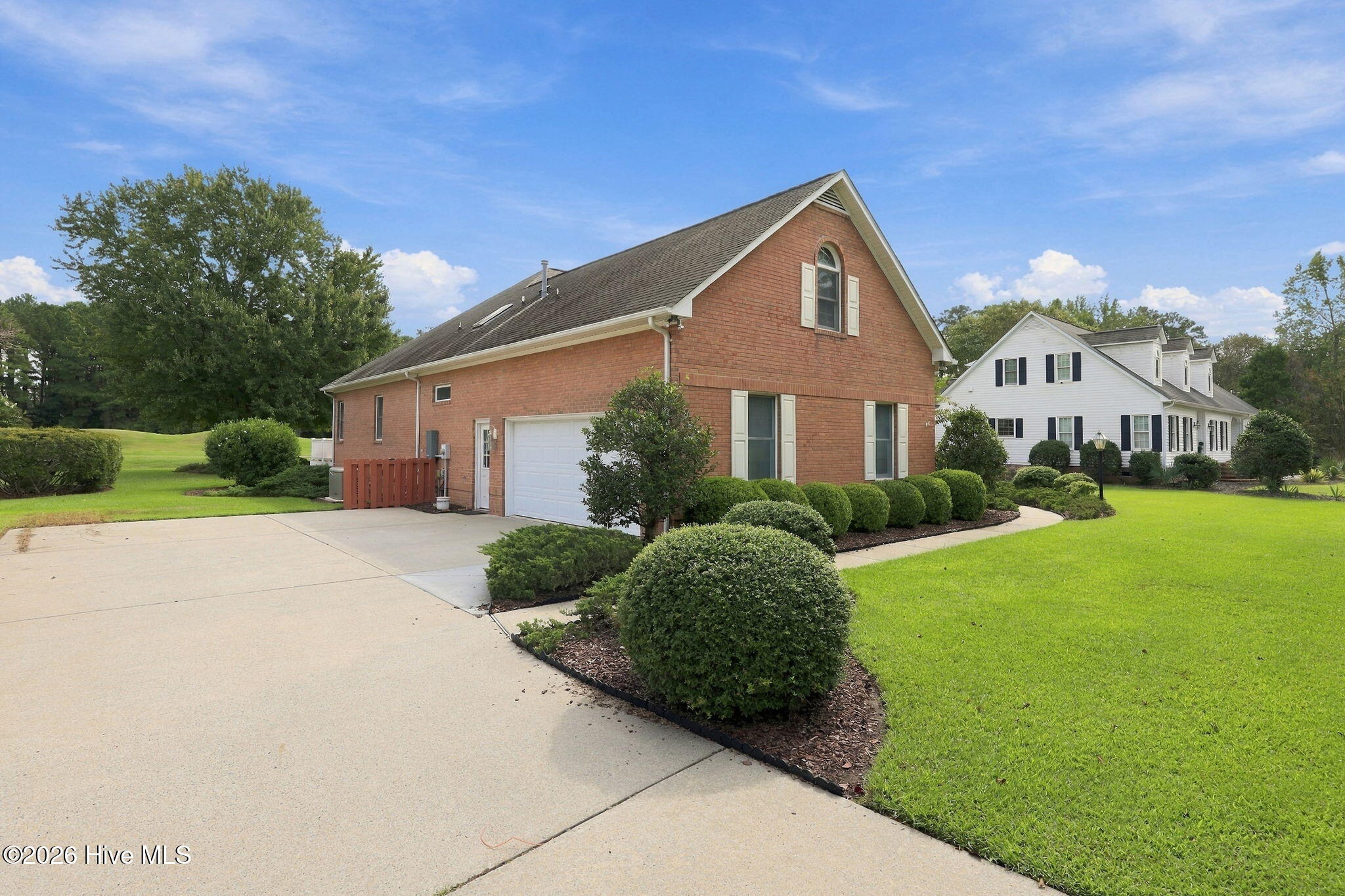 Two-story brick house with an attached garage, broad driveway, and neatly landscaped lawn.