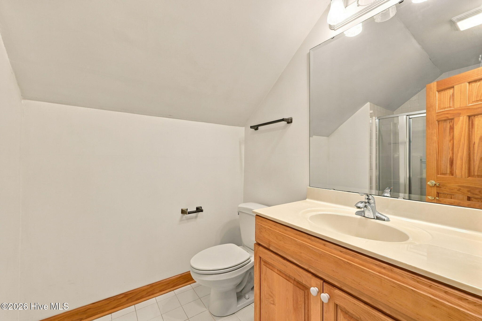 Bathroom with a wood vanity, large mirror, toilet, and glass shower reflected behind it.