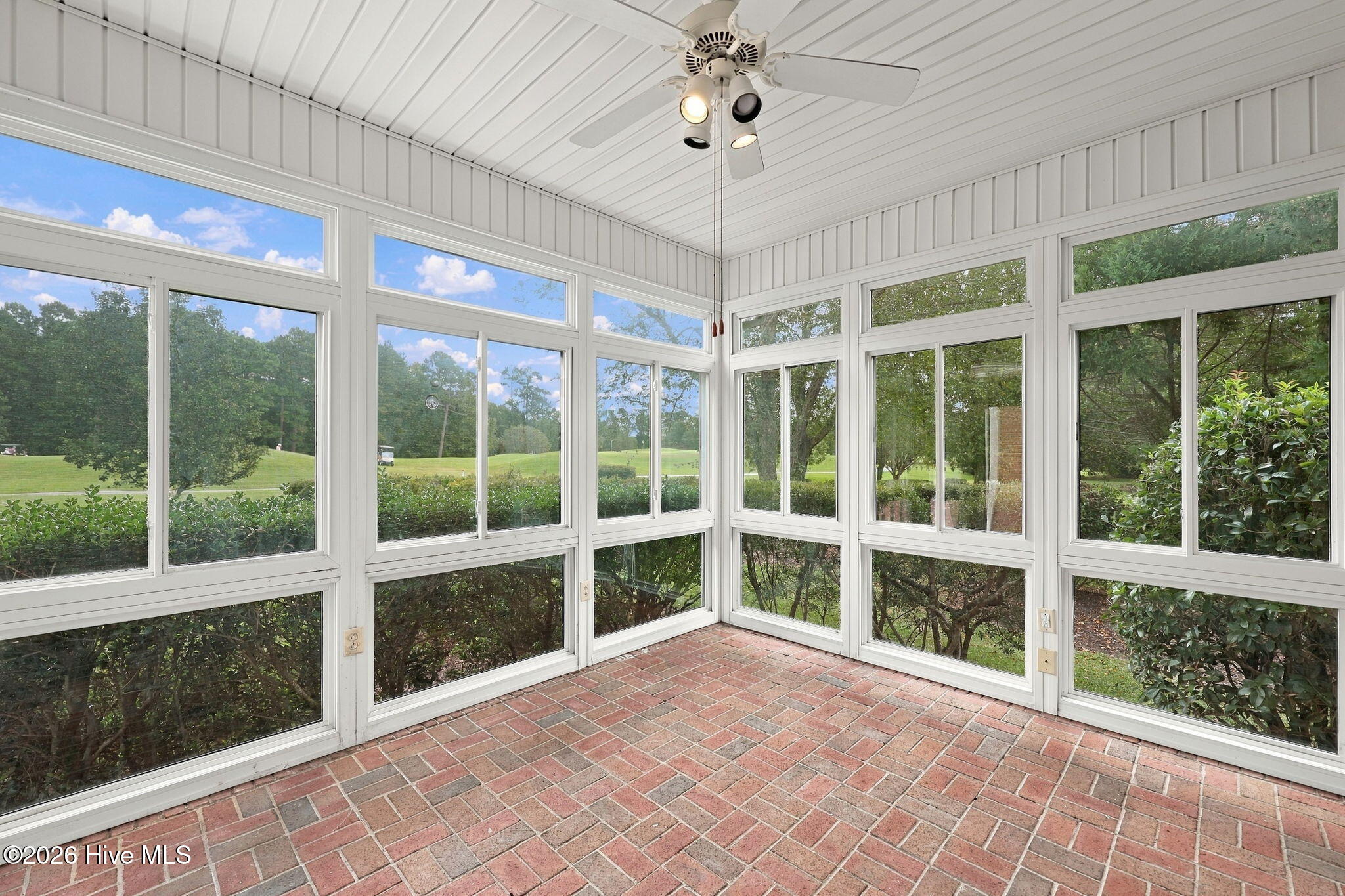Enclosed sunroom with brick flooring, a ceiling fan, and windows overlooking a manicured golf course.