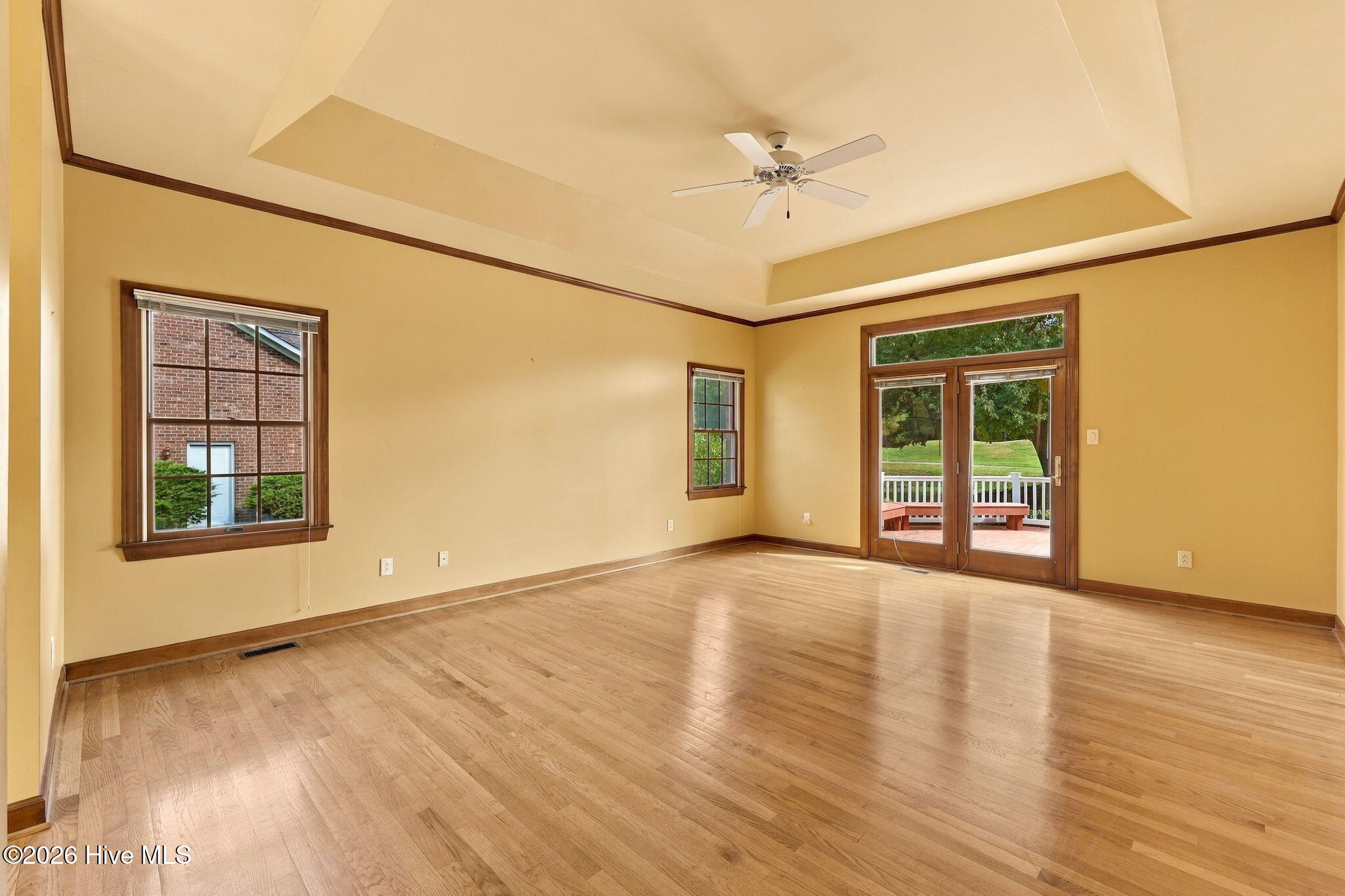 Empty living room with hardwood floors, a tray ceiling, and French doors opening onto a deck.
