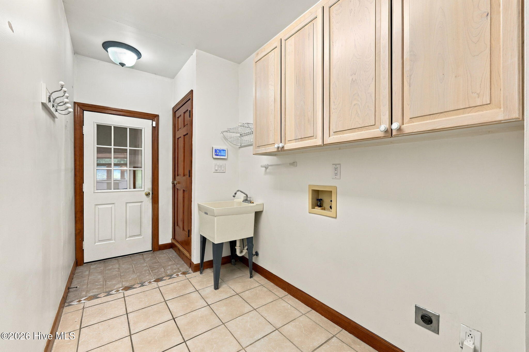 Laundry room with a utility sink, extensive upper cabinets, and tiled flooring.