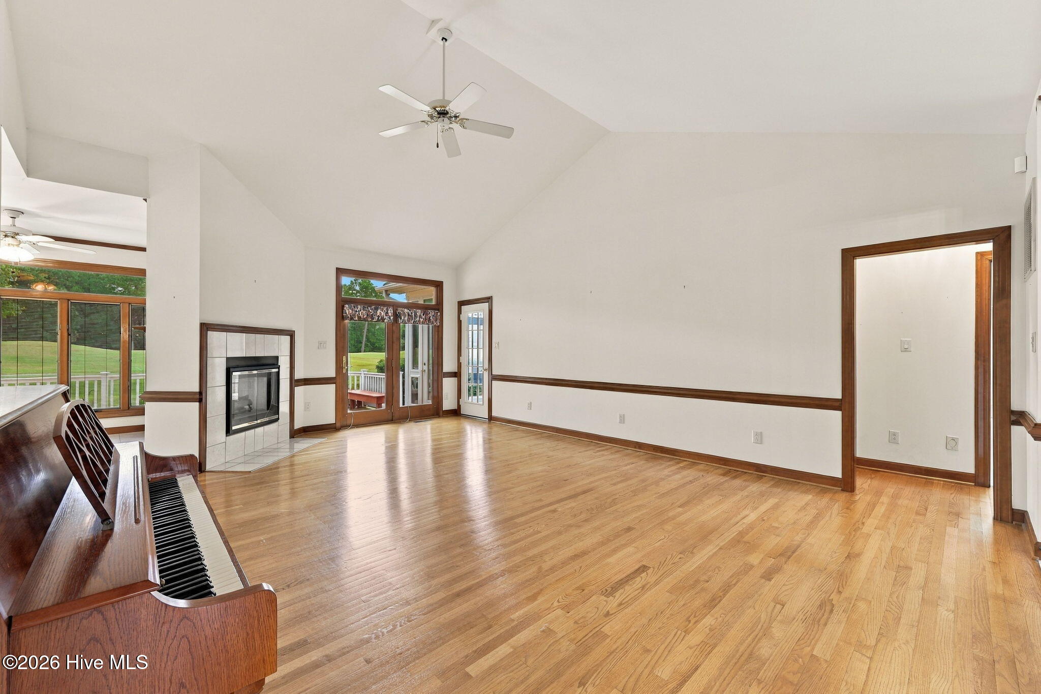 Living room with hardwood floors, vaulted ceiling, tiled fireplace, and upright piano.