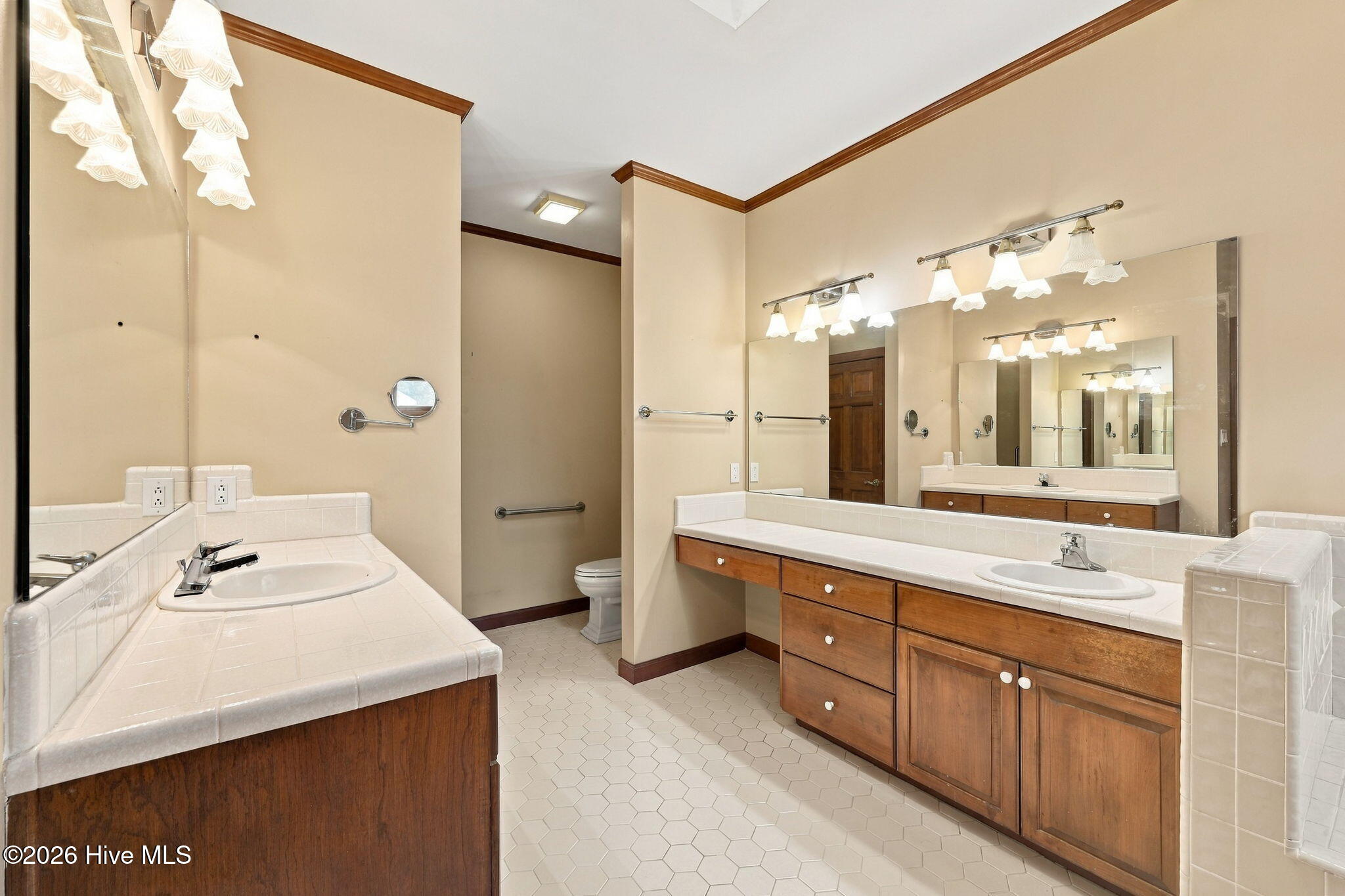 Spacious bathroom with two wood vanities, tiled countertops, large mirrors, and hexagonal floor tiles.