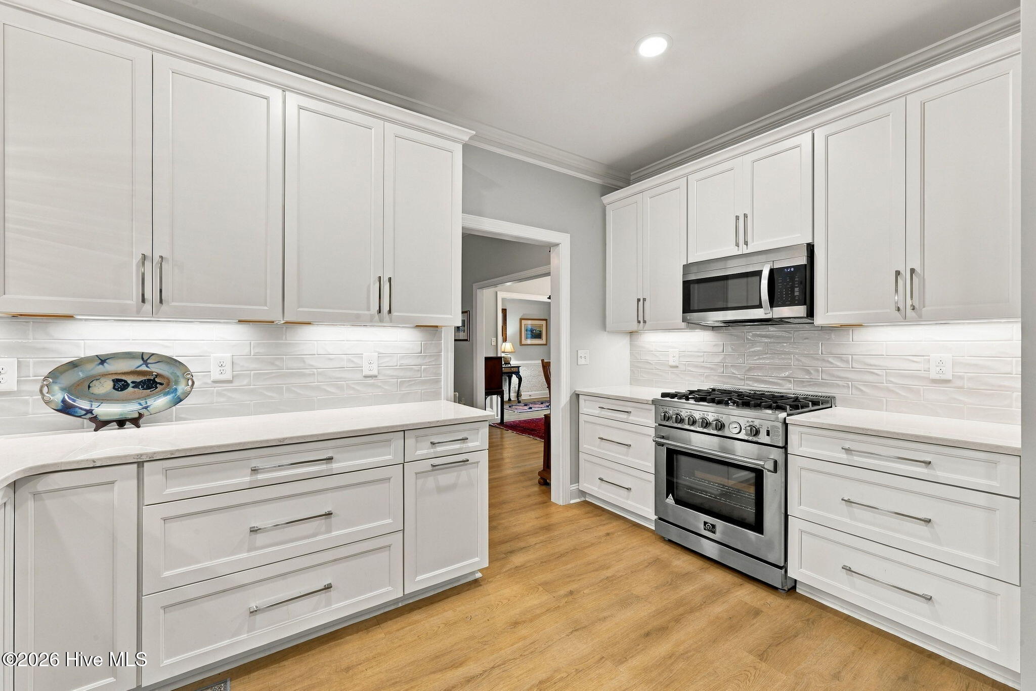 Bright kitchen with white cabinetry, stainless steel appliances, glossy tile backsplash, and warm wood floors.