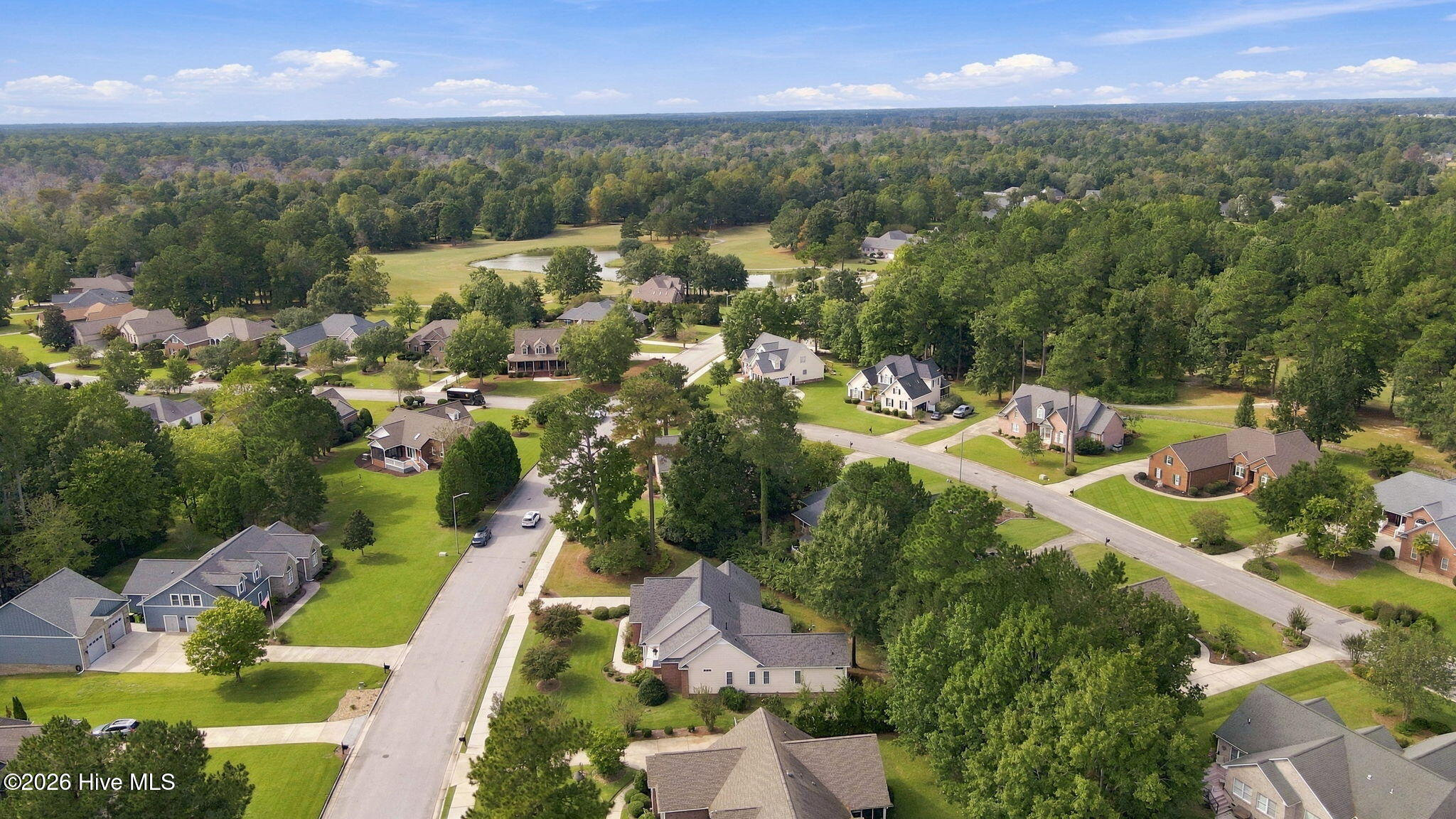 Aerial view of homes beside a golf course, pond, and tree-lined streets.