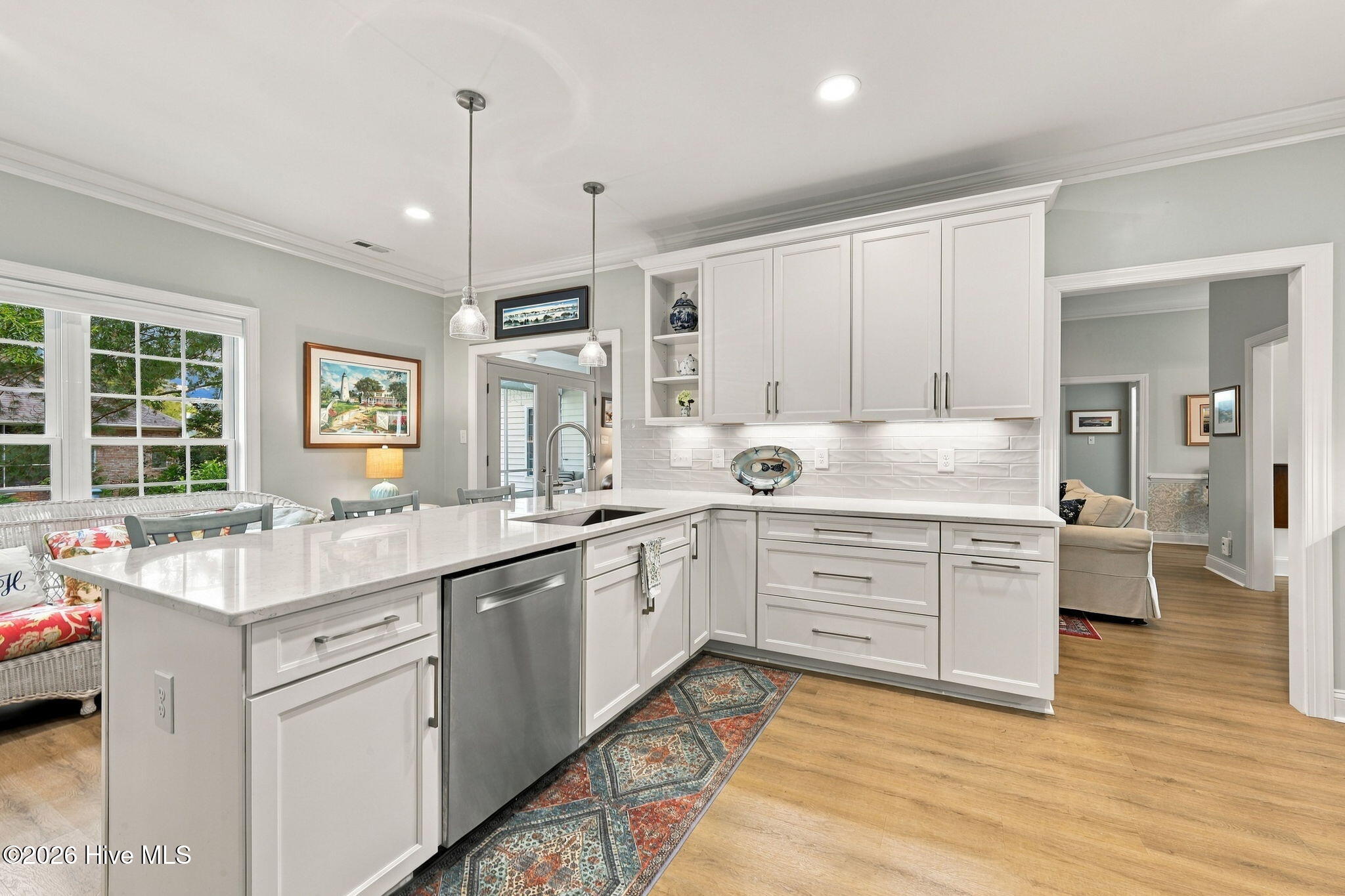 Bright white kitchen with a large island, stainless steel dishwasher, and hardwood floors.