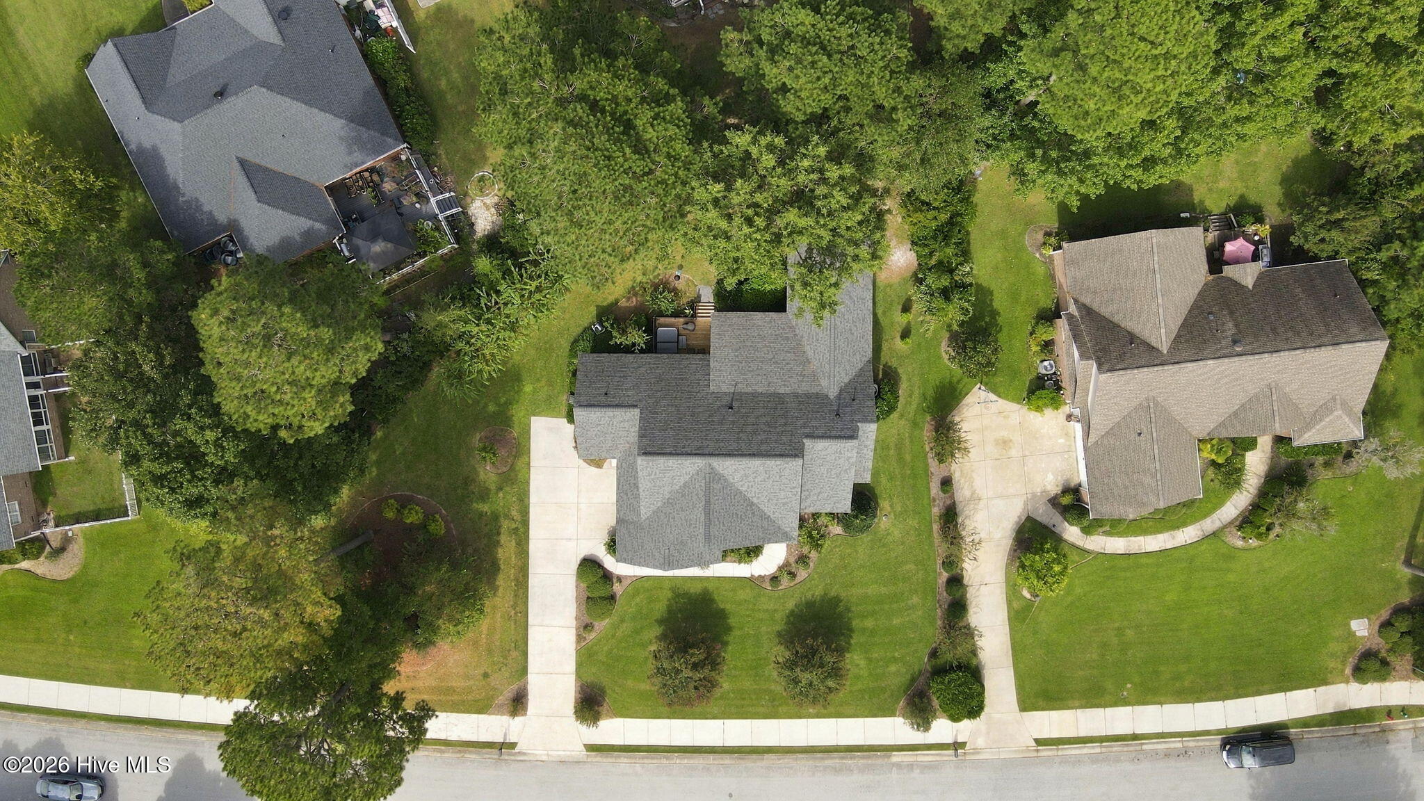 Aerial view of a gray-roofed home with a landscaped lawn, driveway, and mature trees.