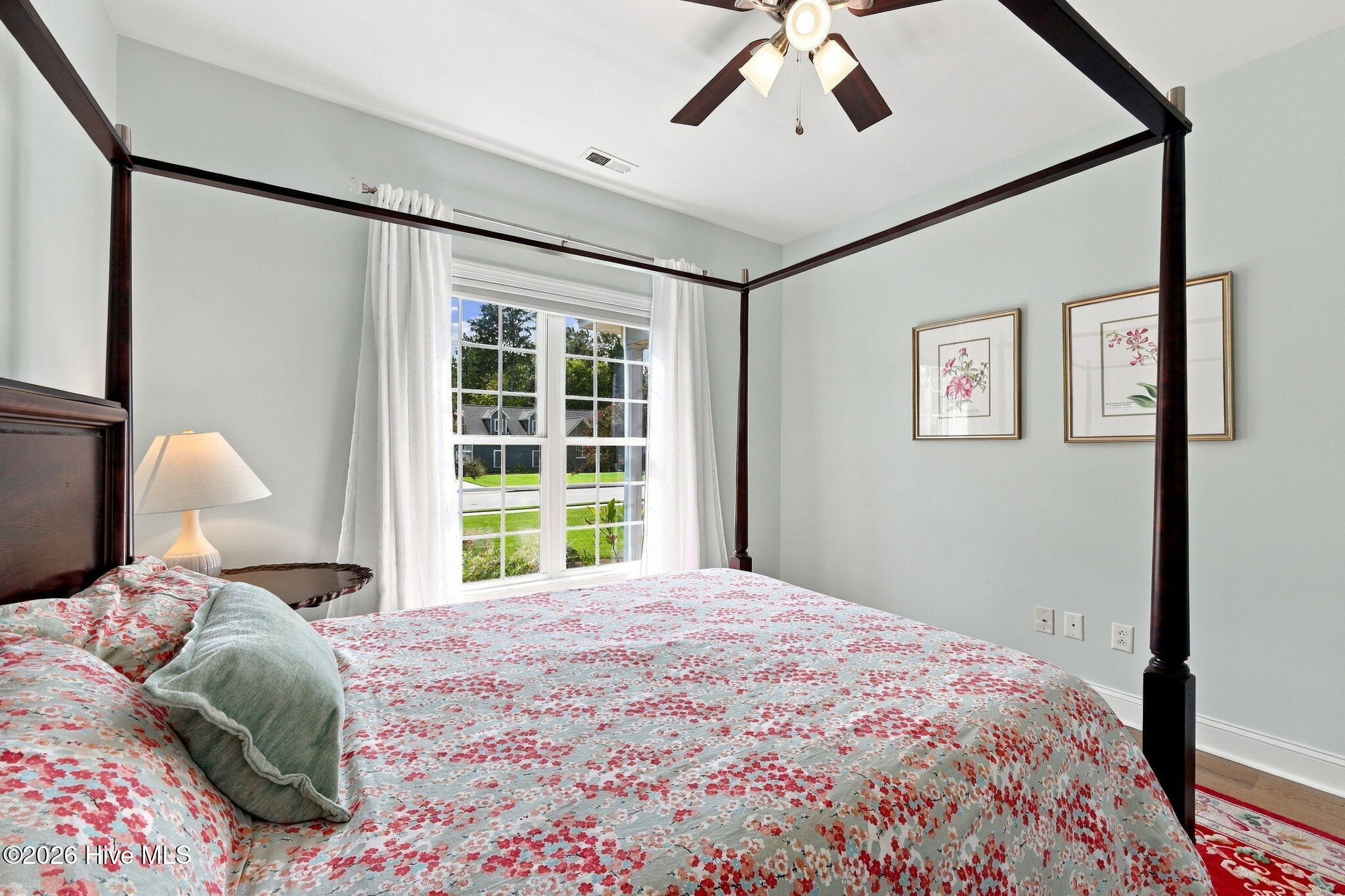 Bedroom with a dark wood canopy bed, floral bedding, and a large curtained window.