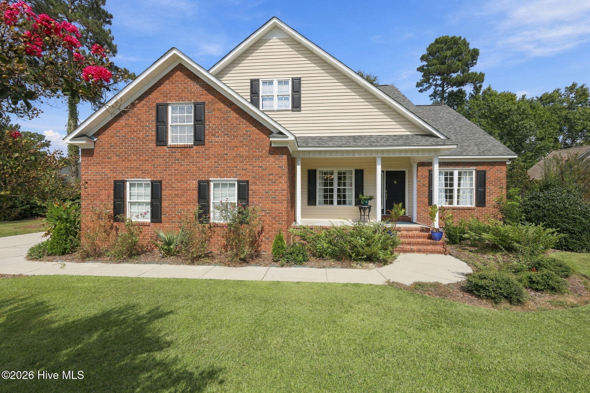 Two-story brick-and-siding home with a covered porch, landscaped front yard, and flowering tree.