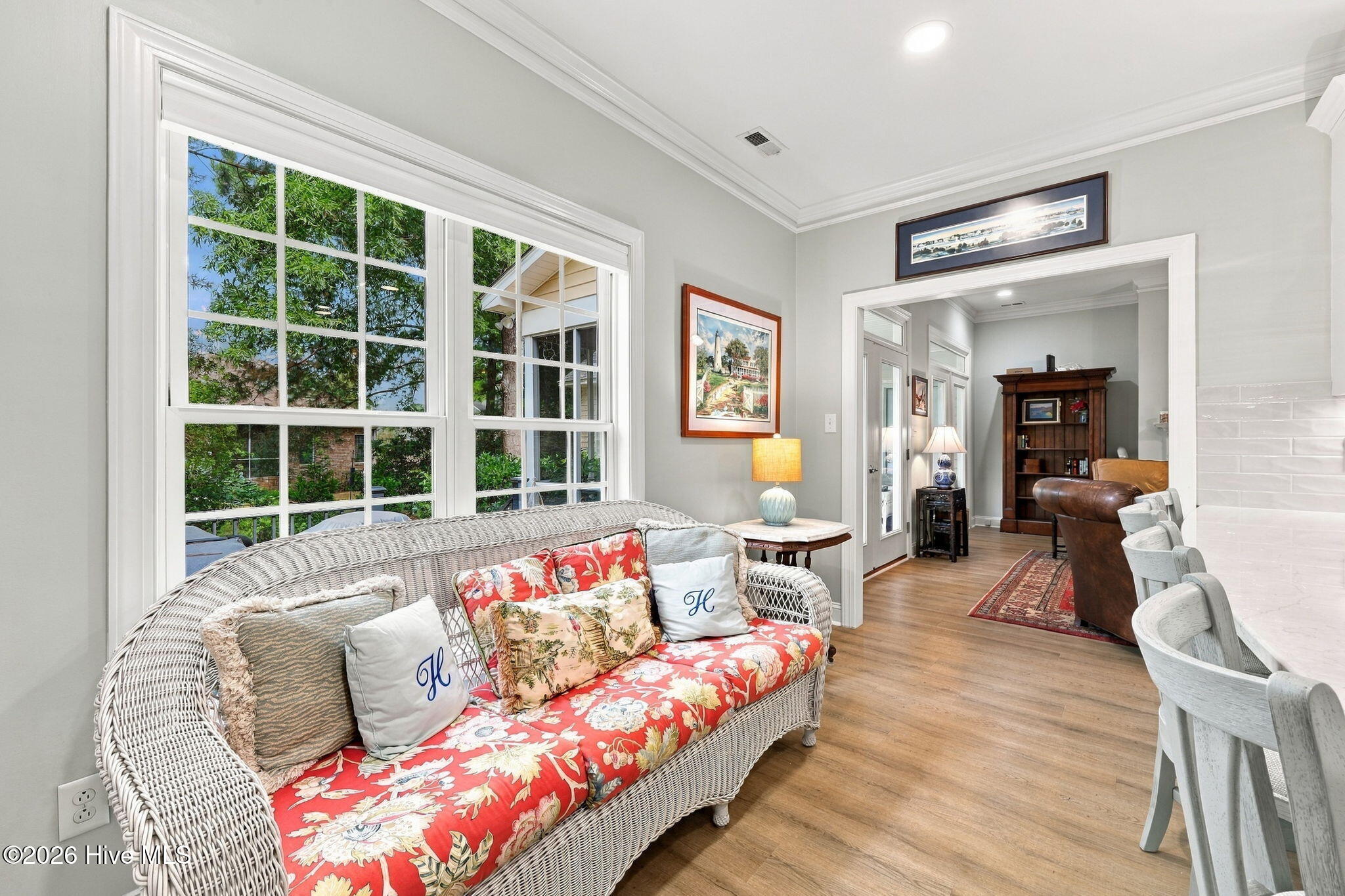 Furnished living area with a floral wicker sofa, large windows, and warm wood floors.