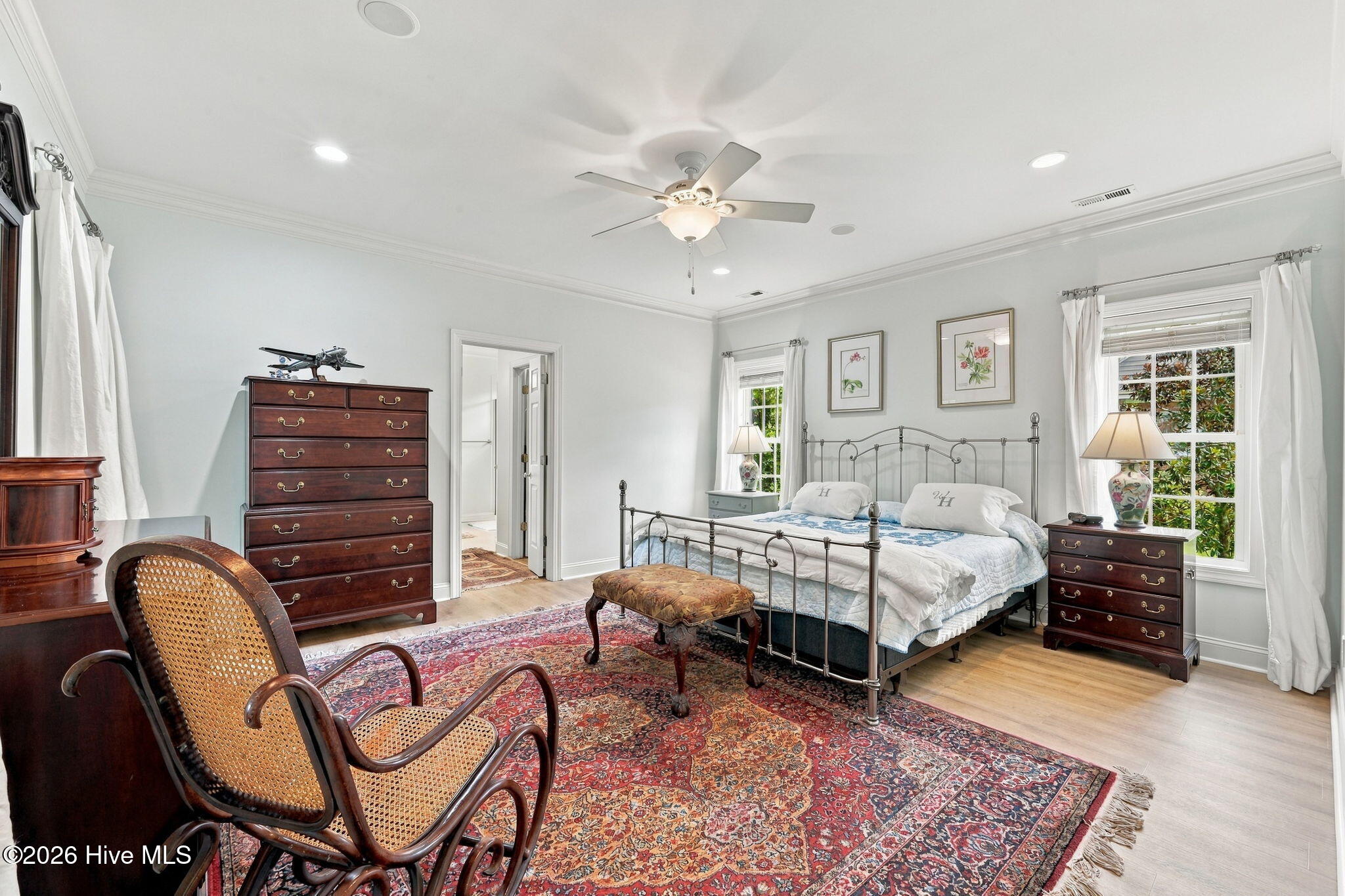 Bedroom with a metal bed, dark wood dressers, cane rocking chair, and large patterned rug.