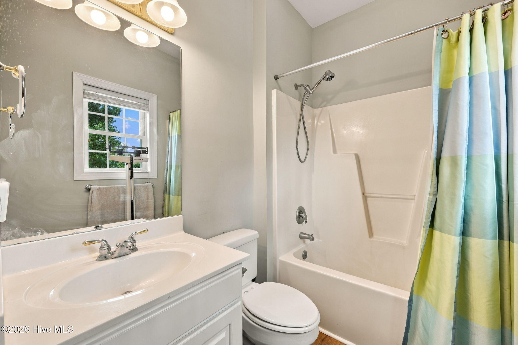 Bathroom with a white vanity, tub-shower, window, and blue, green, and yellow striped shower curtain.