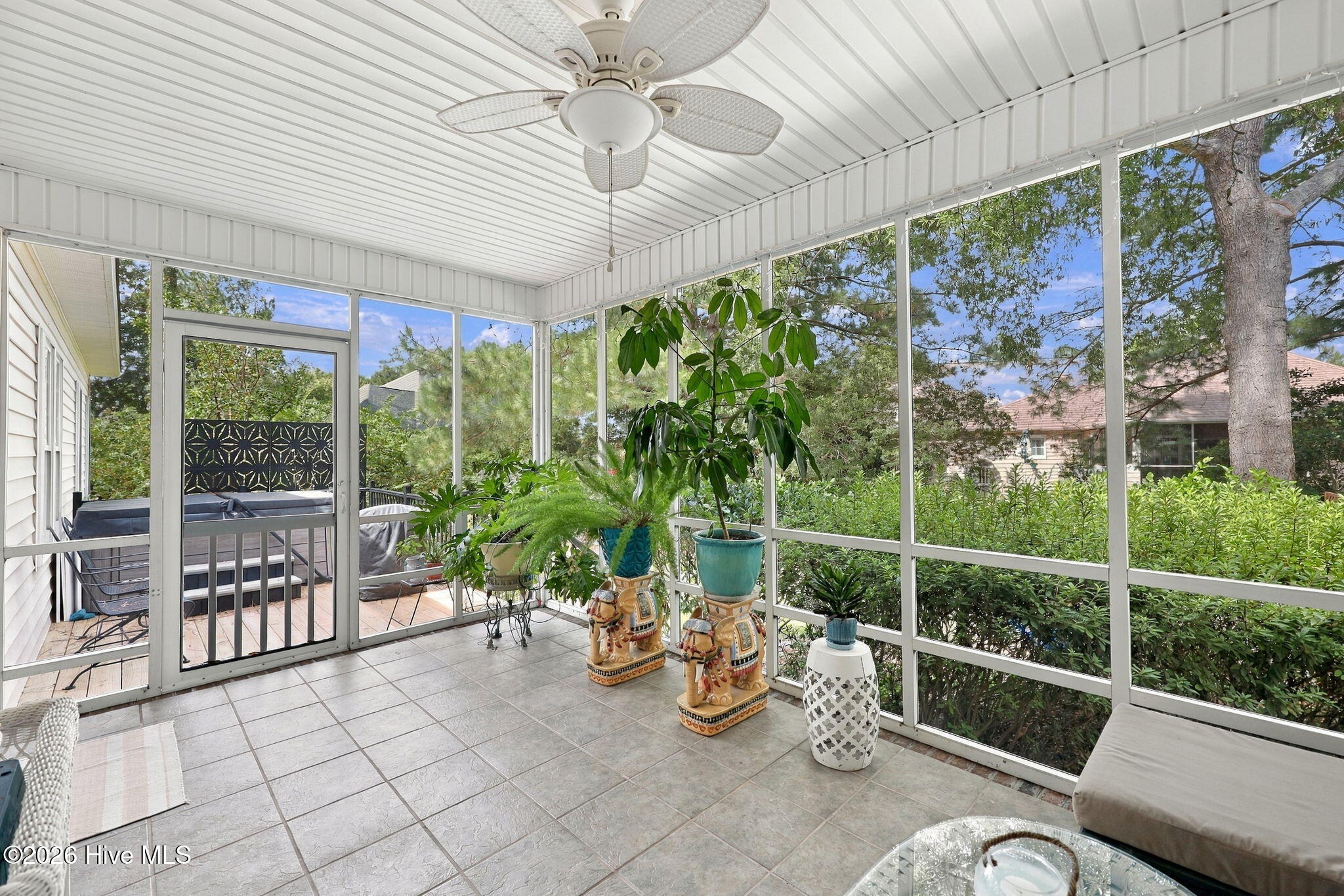 Enclosed porch with tiled floors, a ceiling fan, potted plants, and views of leafy greenery.