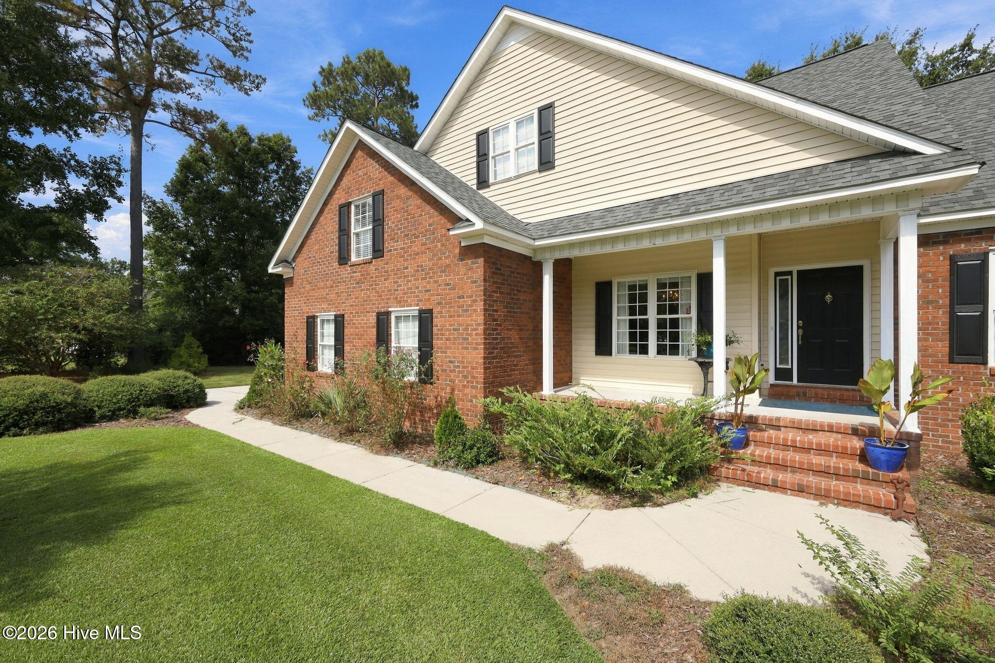 Two-story brick-and-siding home with a covered porch, brick steps, and landscaped front lawn.