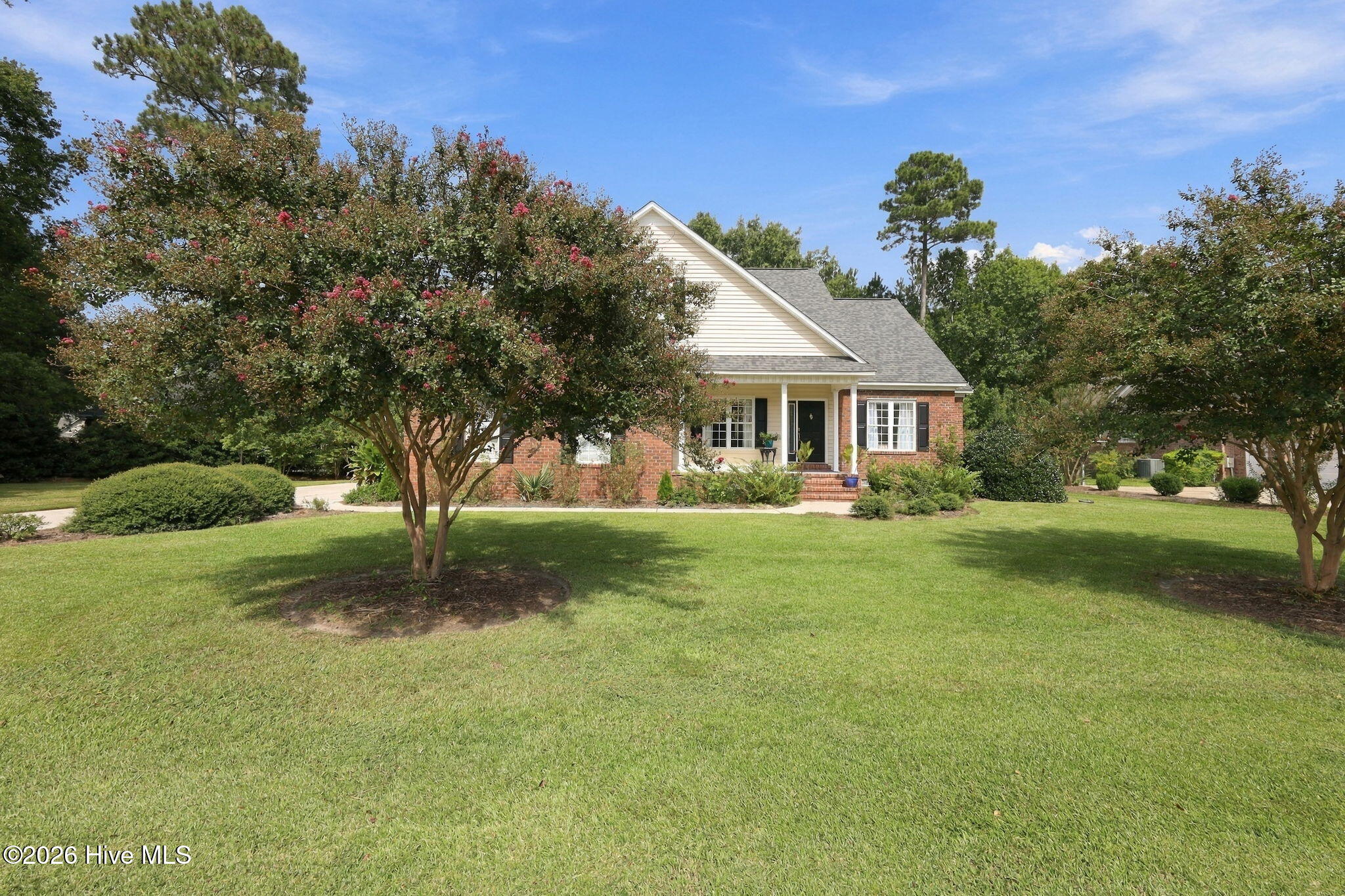 Brick home with a covered entry, broad lawn, and flowering trees.