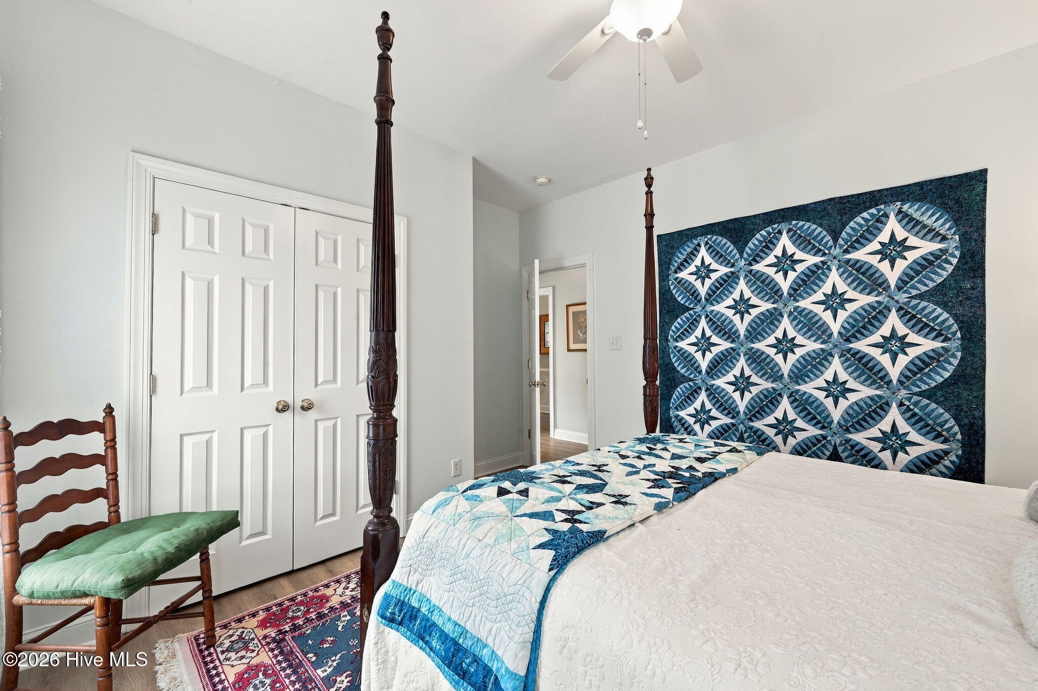 Bedroom with a blue geometric quilt headboard, carved four-poster bed, and wooden chair with green cushion.