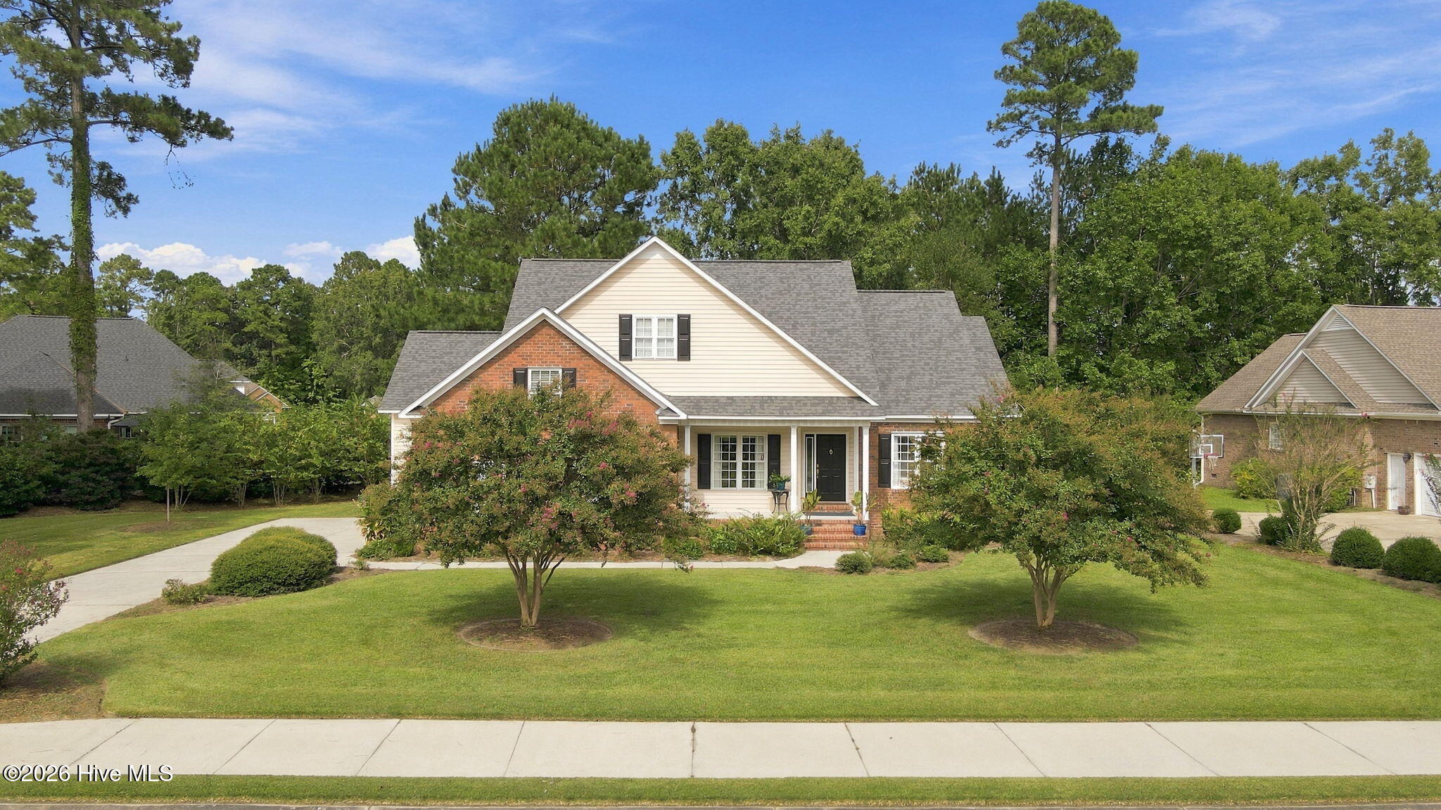 Two-story brick and cream-sided home with dark shutters, landscaped lawn, and curved driveway.