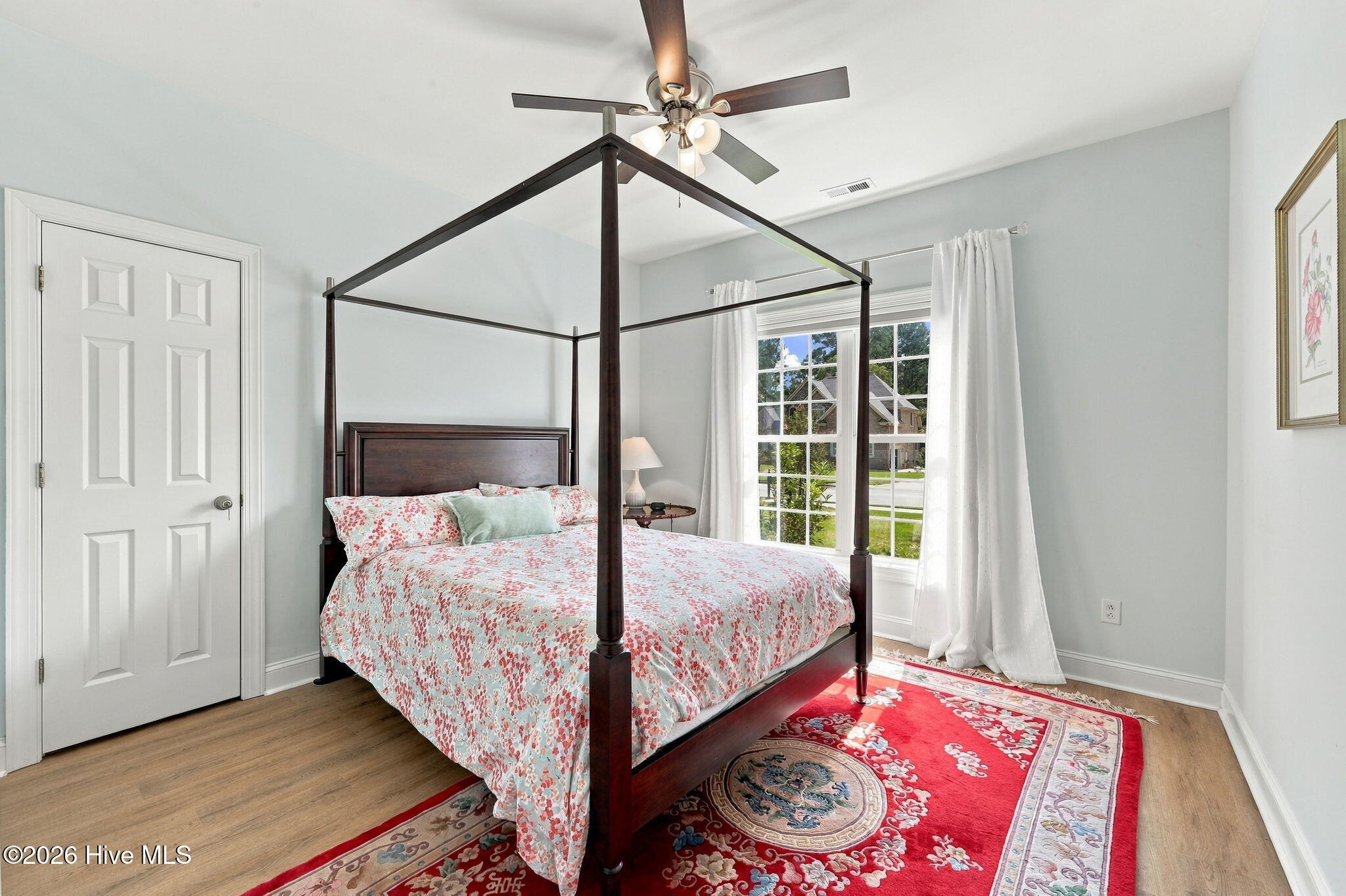 Bedroom with a dark wood four-poster bed, floral bedding, and a red patterned rug.