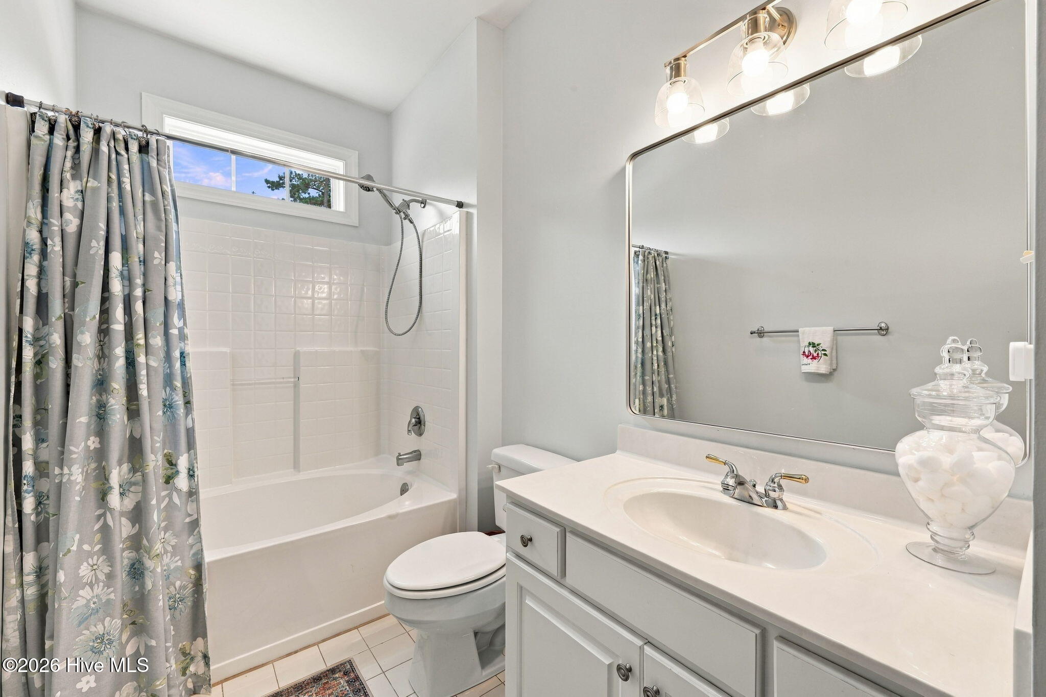 Bathroom with a white tub, floral shower curtain, and long vanity beneath a large mirror.