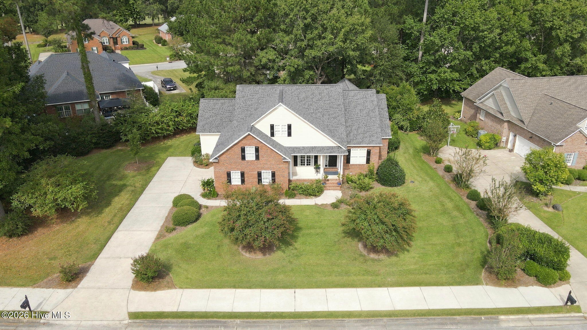 Aerial view of a two-story brick-and-white home with a gray roof and landscaped front lawn.