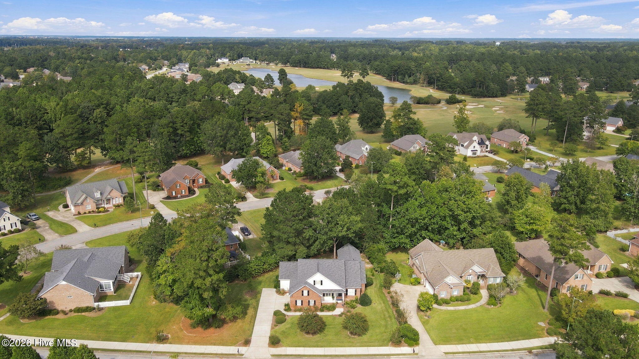 Aerial view of homes beside a golf course, ponds, and wooded landscape.