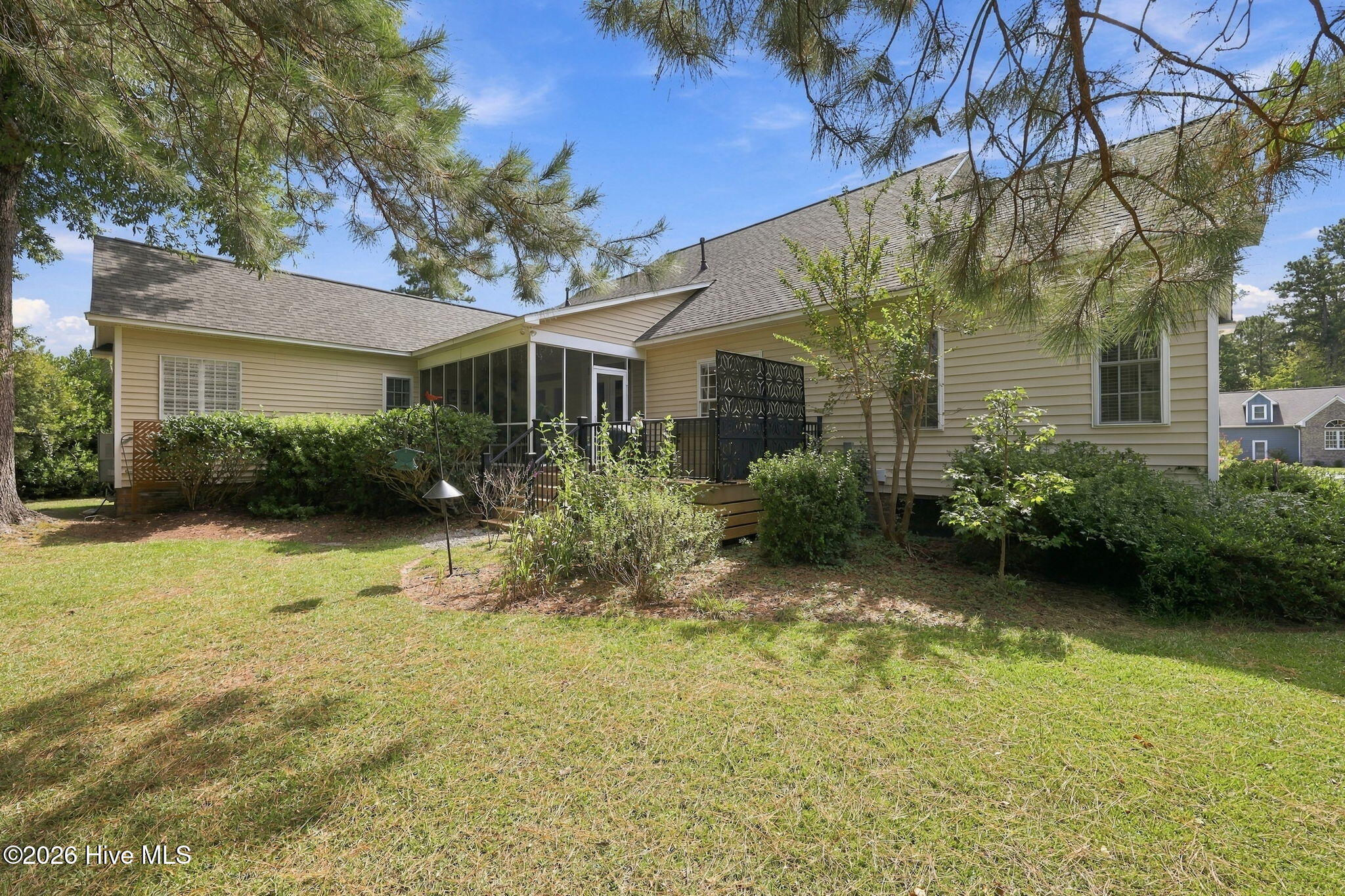 Rear of beige-sided home with screened porch, raised deck, and landscaped lawn.