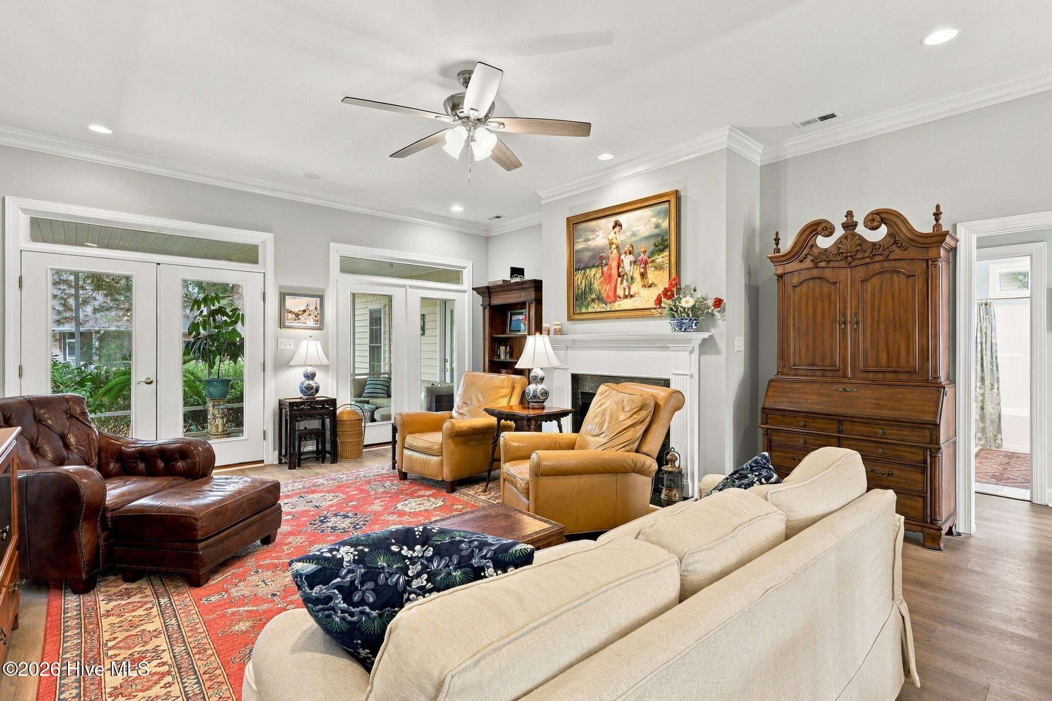 Furnished living room with a white fireplace, leather armchairs, and an ornate wooden cabinet.