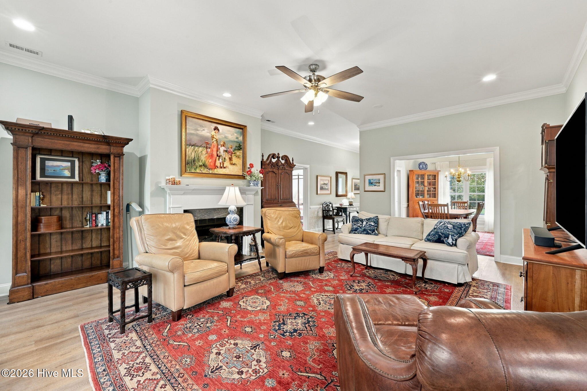 Furnished living room with a white fireplace, leather chairs, cream sofa, and large red patterned rug.