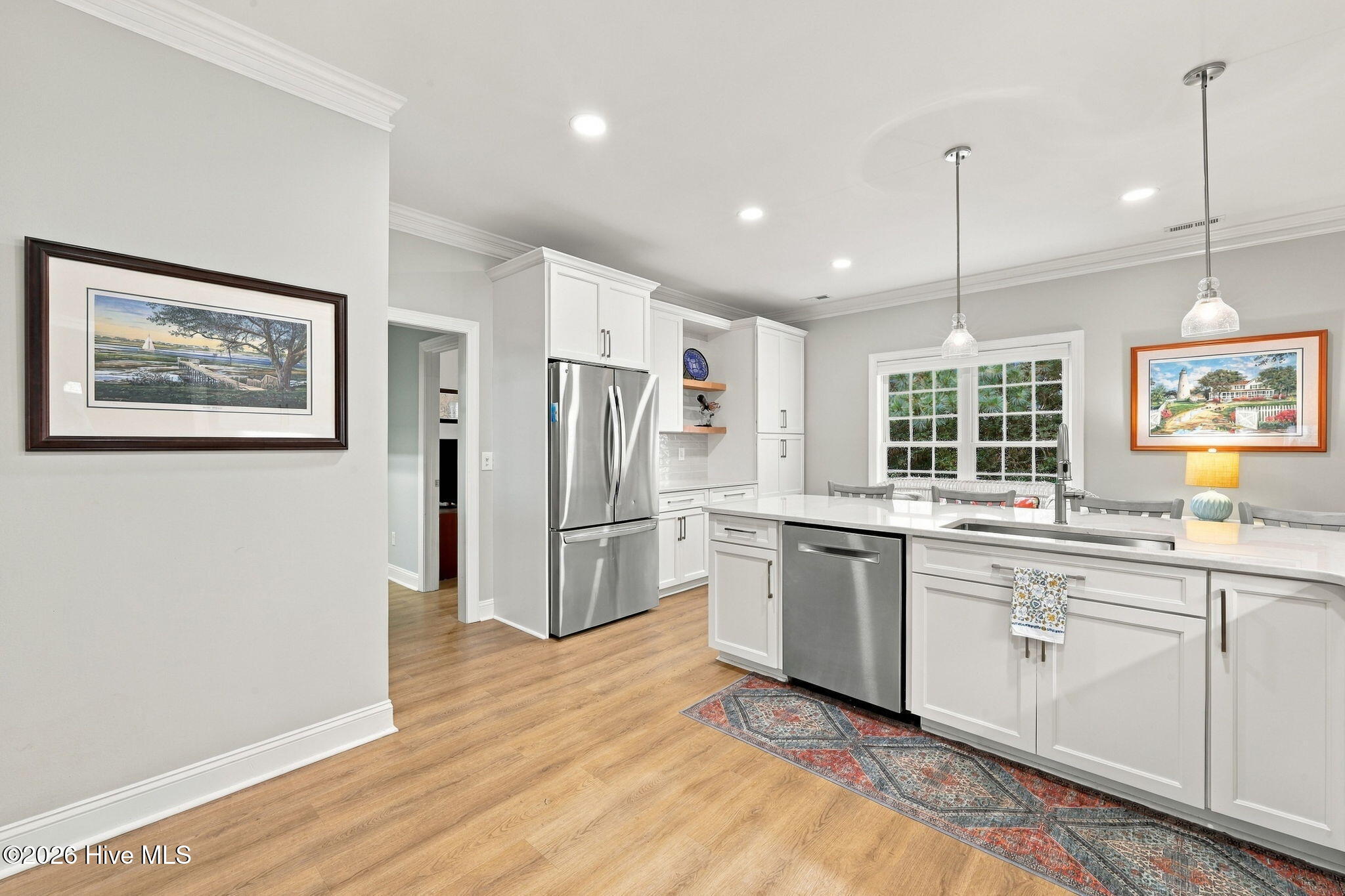 Bright white kitchen with stainless steel appliances, a large island, and light wood flooring.
