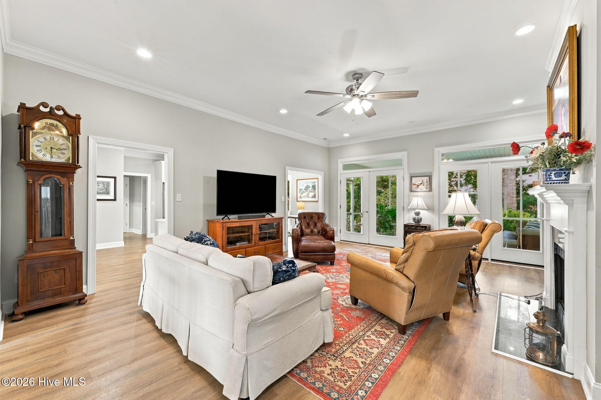 Furnished living room with leather seating, a red patterned rug, hardwood floors, and glass doors to greenery.