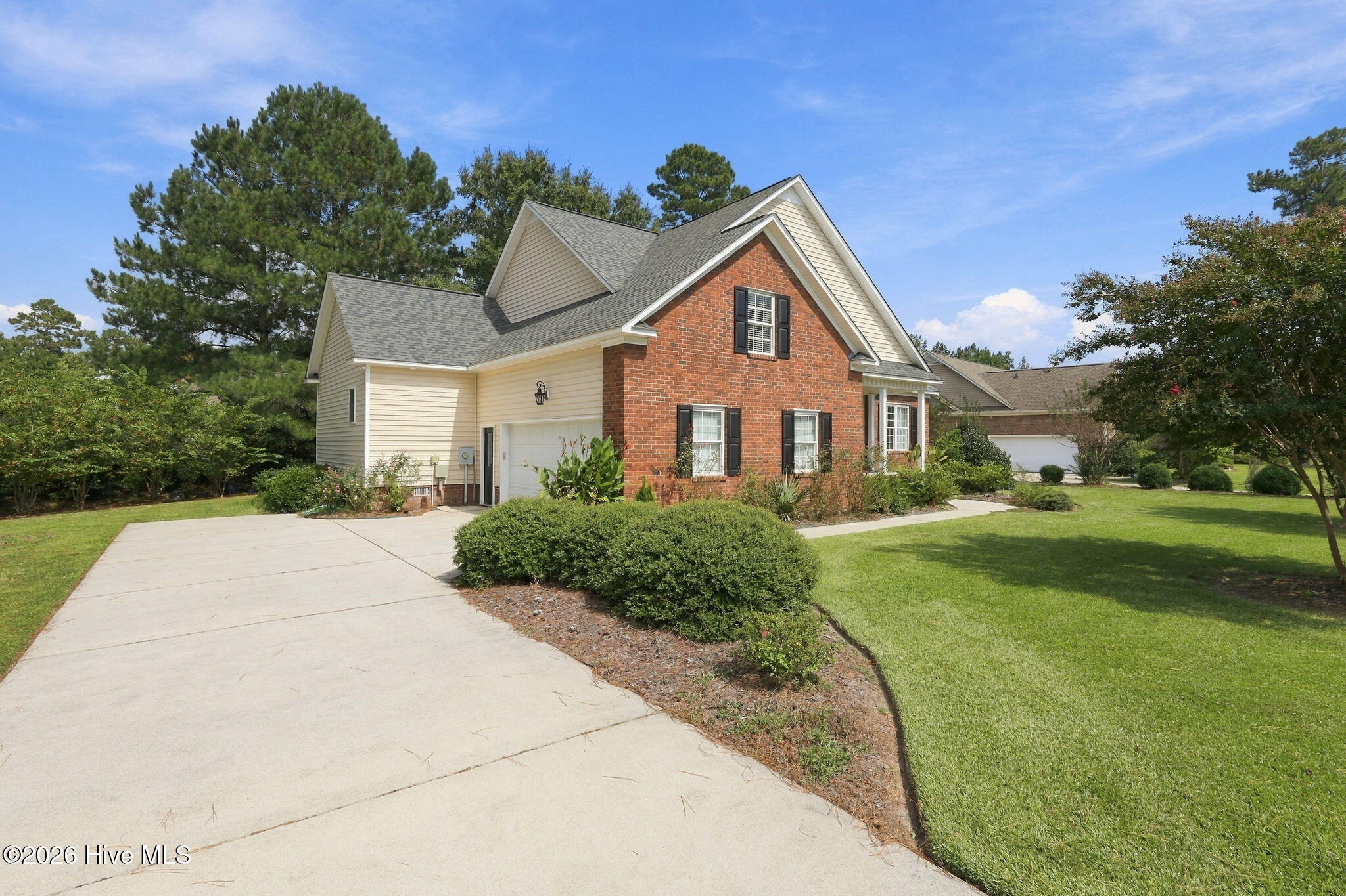 Two-story brick-and-siding home with an attached garage, landscaped lawn, and broad concrete driveway.