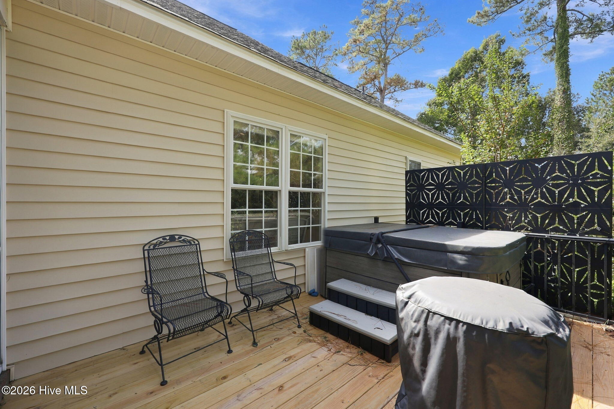 Wooden deck with a covered hot tub, metal chairs, and decorative privacy screens beside the home.