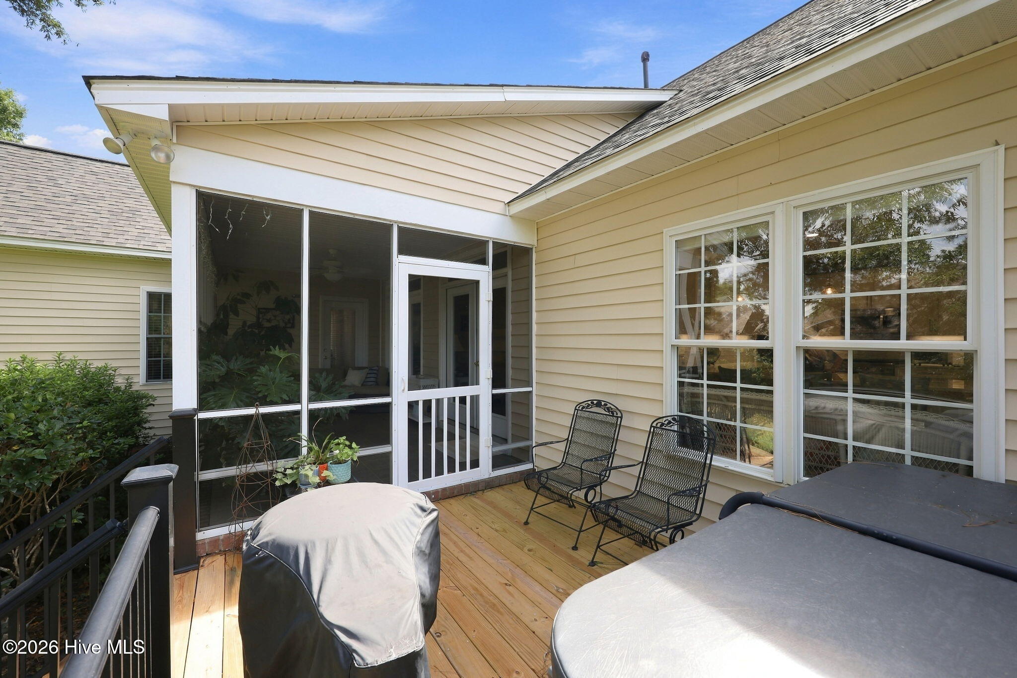 Wood deck beside a screened porch, with metal chairs and covered outdoor furniture.