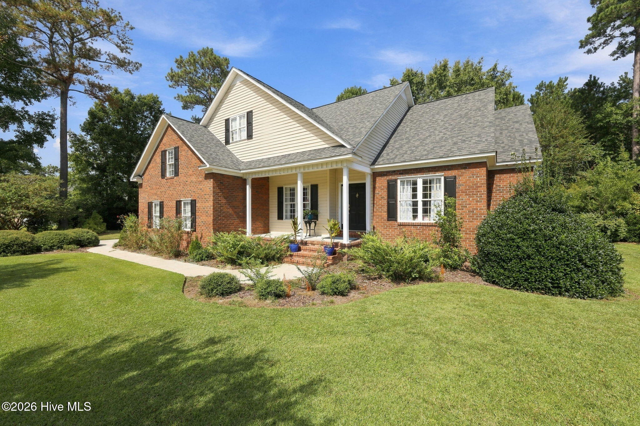 Two-story brick and cream-sided home with a covered porch, gabled roof, and landscaped front lawn.