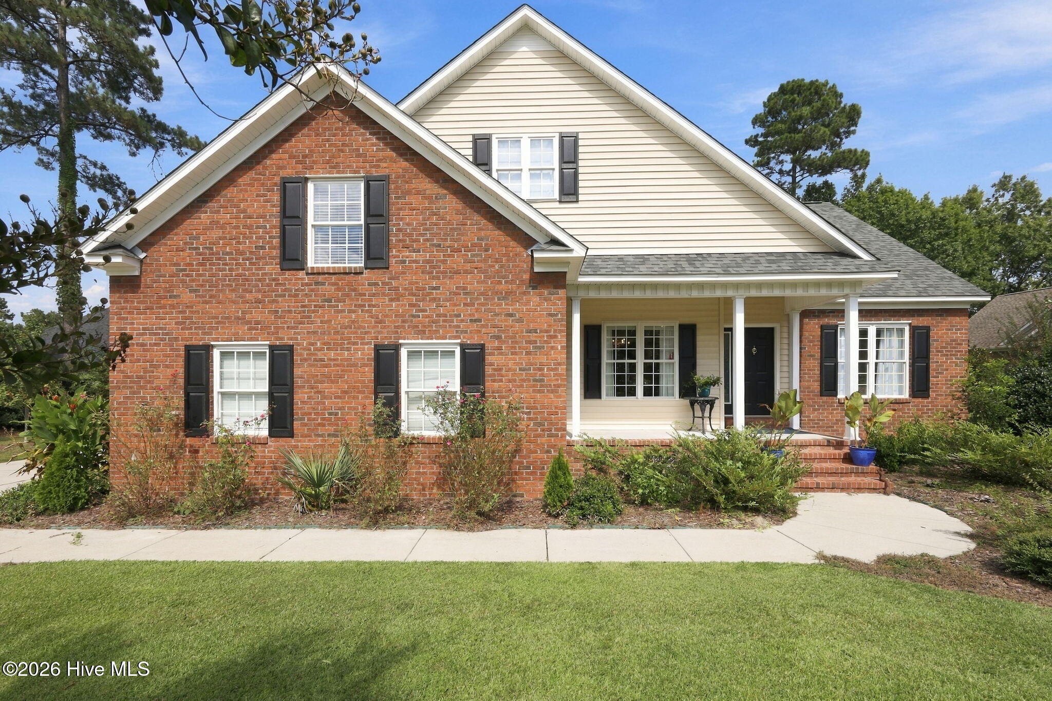 Two-story brick-and-siding home with black shutters, a covered porch, and landscaped front lawn.