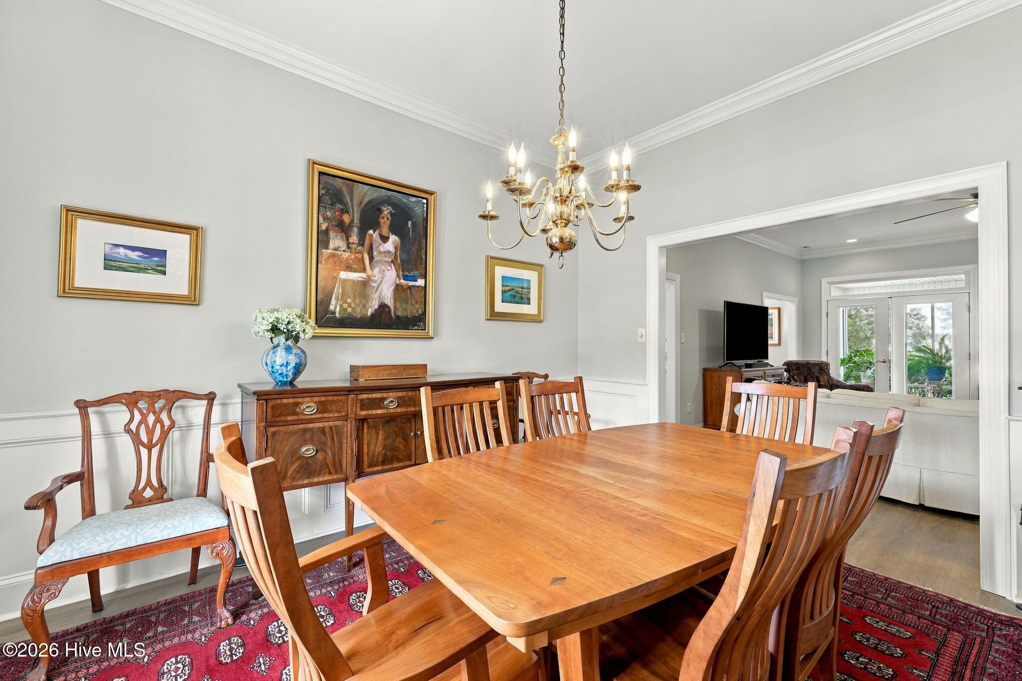 Dining room with a large wooden table, red patterned rug, and brass chandelier.