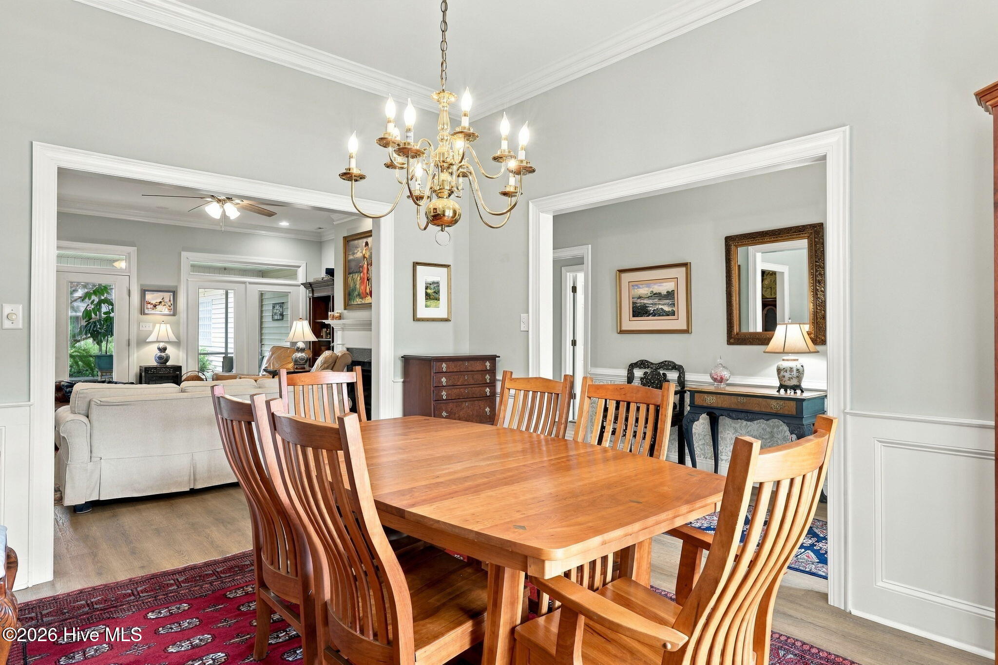 Dining room with a wooden table and chairs beneath a brass chandelier, opening onto the living room.