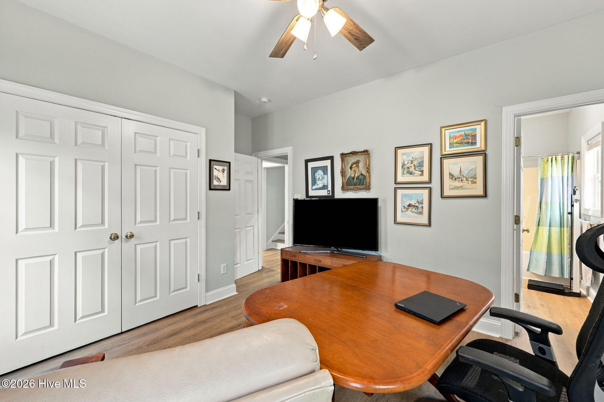 Home office with a large wooden desk, framed artwork, and an adjoining bathroom visible through the doorway.