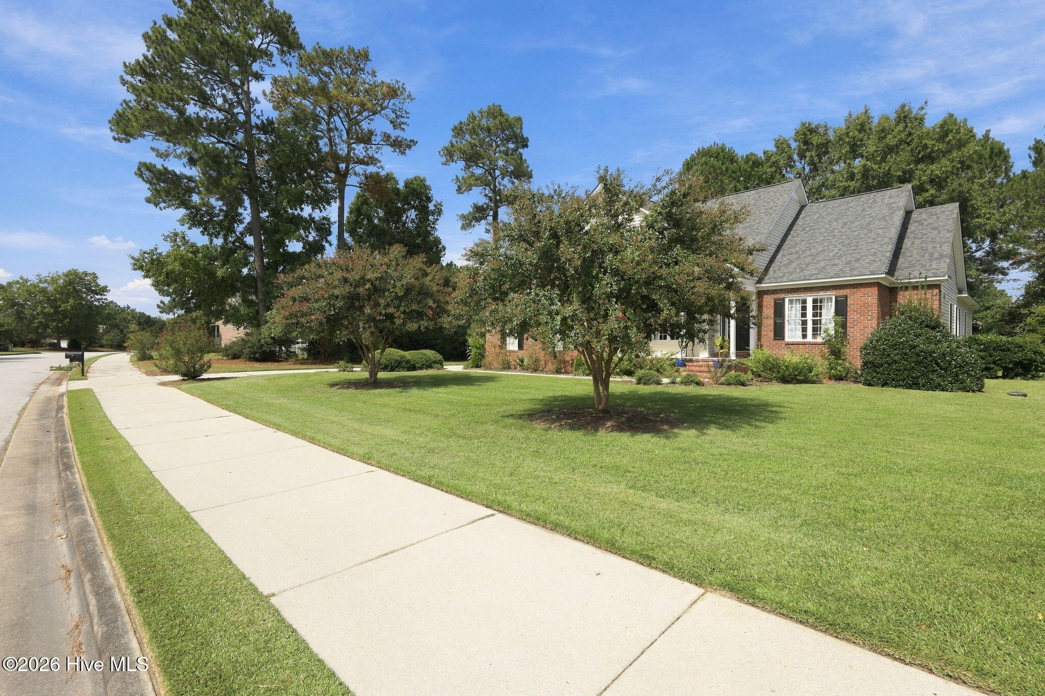 Brick-and-siding house with a steep gray roof, black shutters, and a landscaped lawn beside the sidewalk.