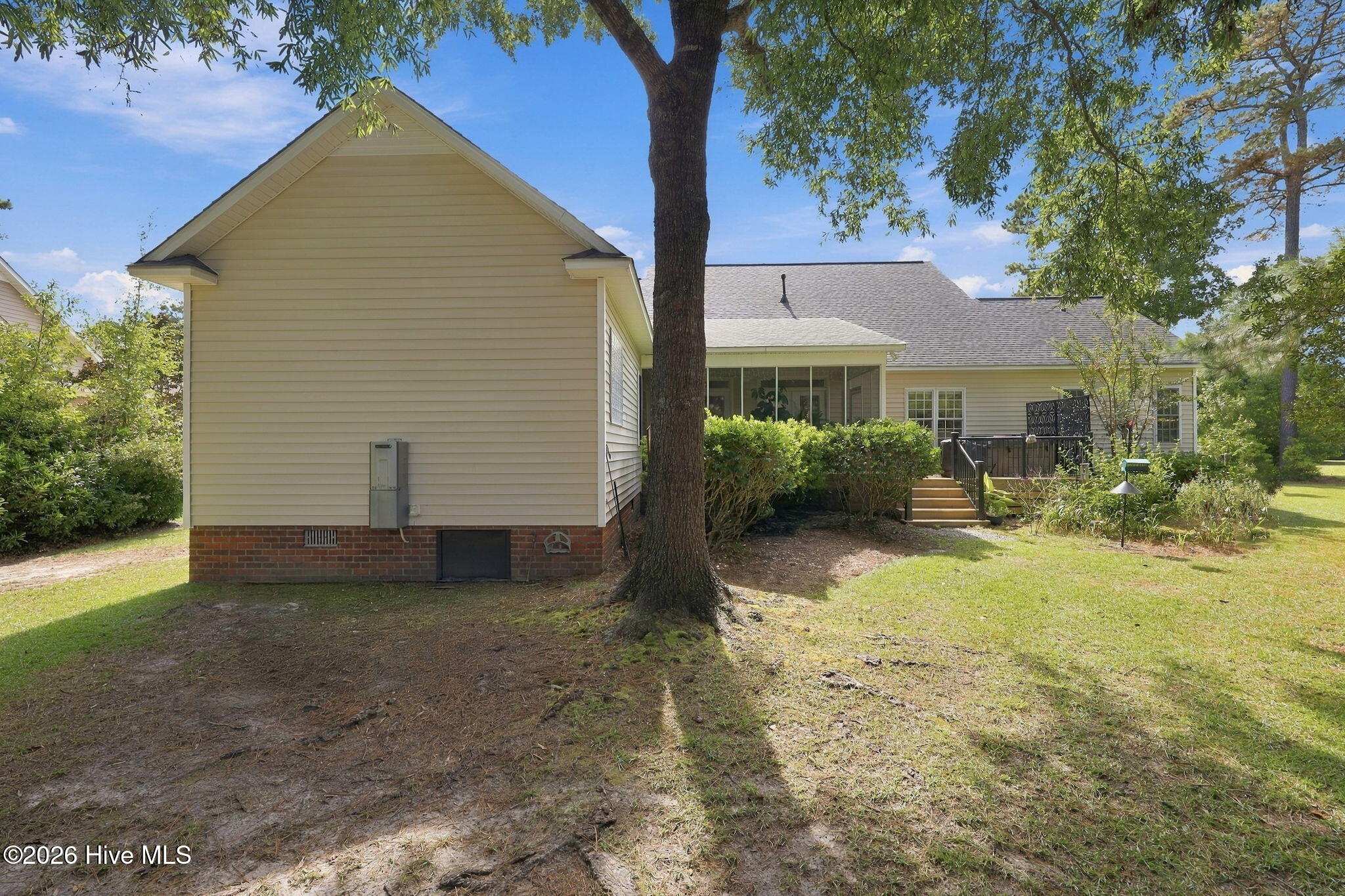 Rear of a beige-sided house with a screened porch, deck steps, and a large tree in the yard.