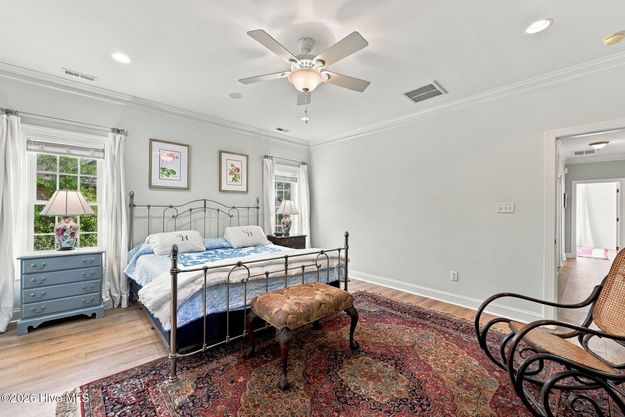 Furnished bedroom with a black metal bed, blue-and-white bedding, patterned rug, and windows with white curtains.