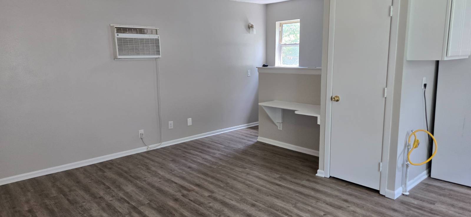 Empty room with dark wood-look flooring, a window air conditioner, and a small built-in counter.