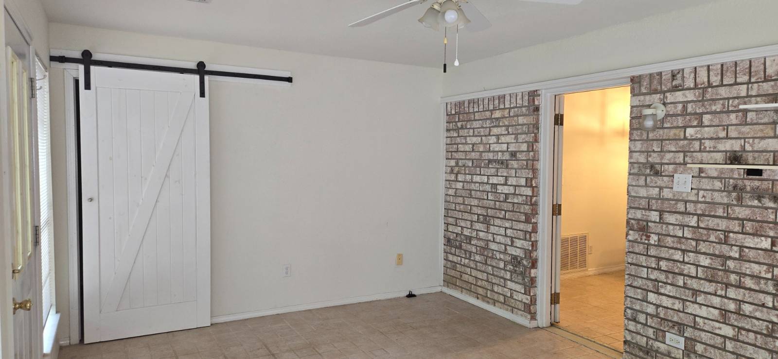 Empty room with brick walls, tiled floor, and a white sliding barn door.