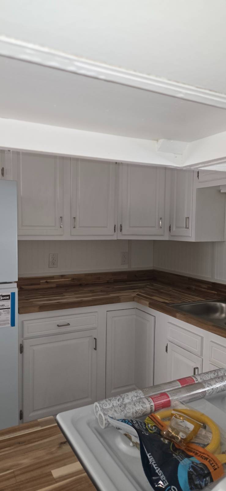 Kitchen with white paneled cabinets, wood-look countertops, and renovation supplies piled in the foreground.
