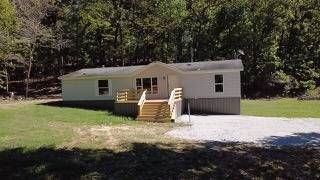 Single-story home with wooden entry steps and a broad gravel driveway beside a wooded area.